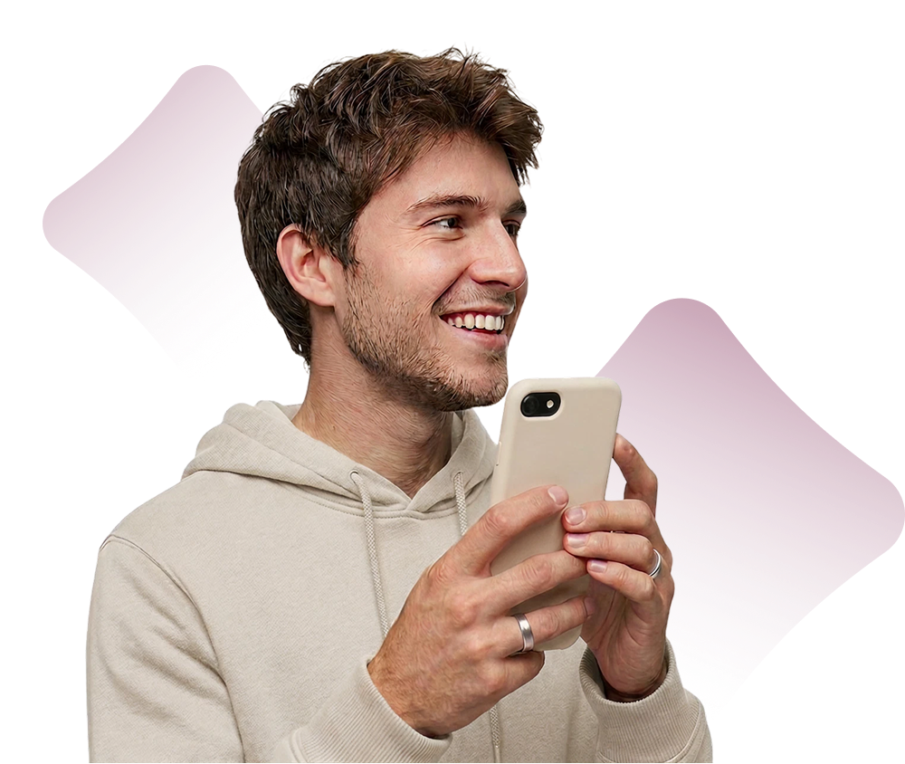 Smiling young man in beige hoodie holding white smartphone with both hands, looking to the right.