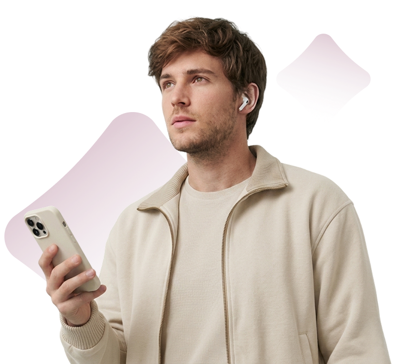 Young man with beige jacket holding smartphone and wearing white wireless earbuds, looking up thoughtfully.