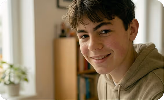 Adolescent souriant avec un sweat à capuche beige dans une pièce bien éclairée.