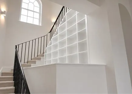Empty white shelves built into stairwell with black railing and large arched window above.