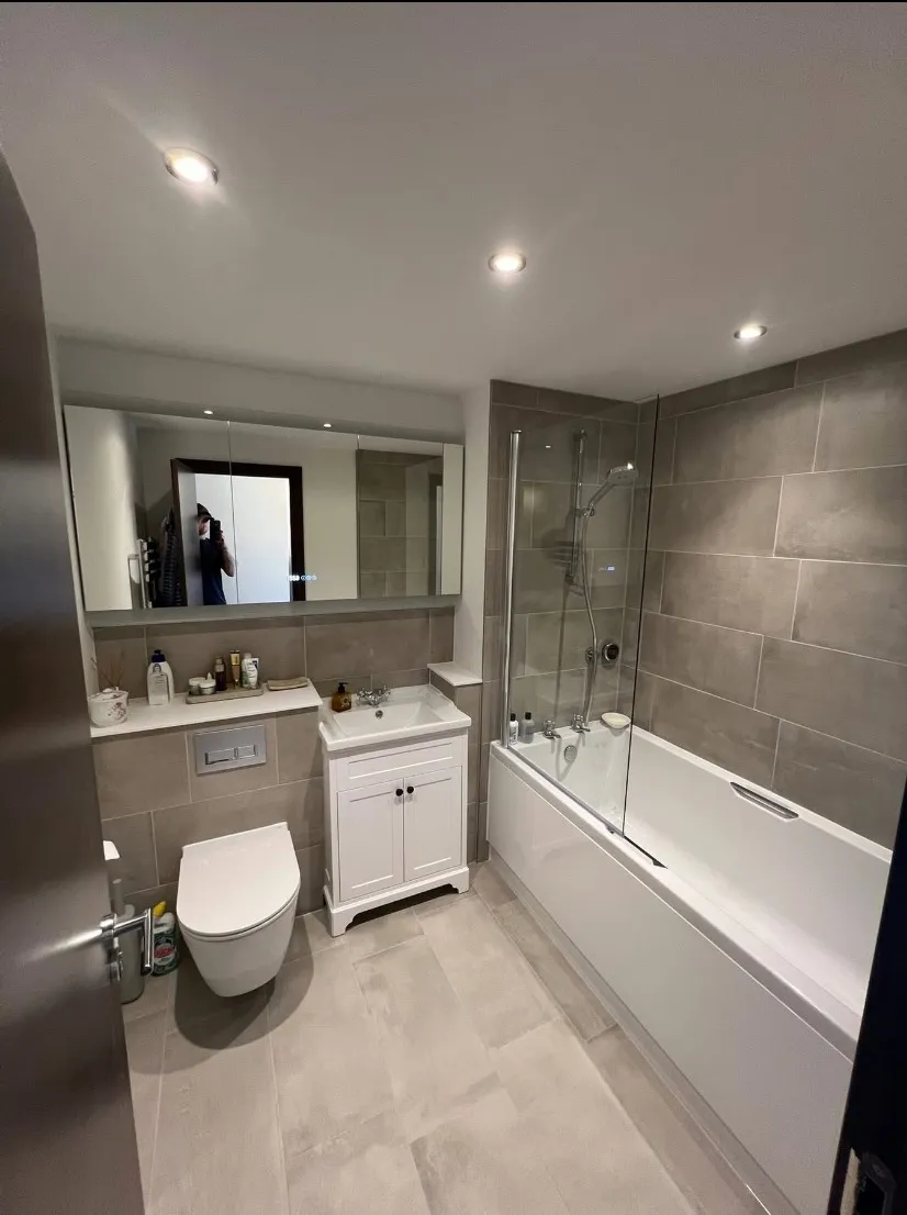 Modern bathroom with bathtub, shower, white vanity, wall-mounted toilet, and mirrored cabinet.