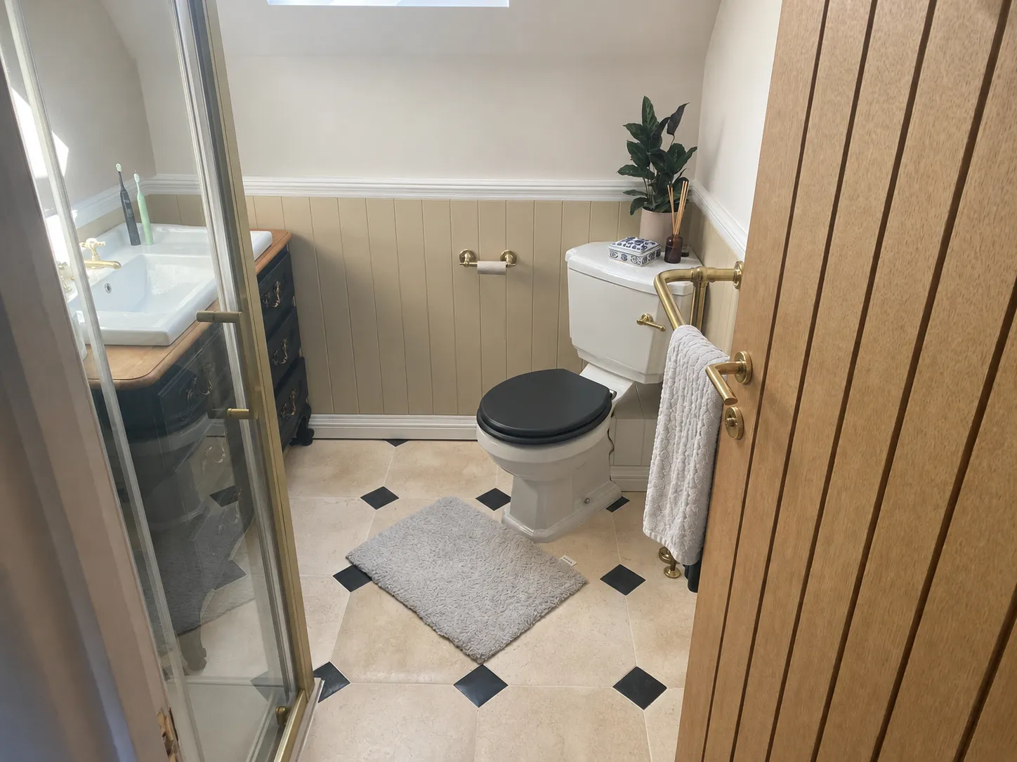 Small bathroom with a black seat toilet, sink, beige walls, and a gray rug on tiled floor.