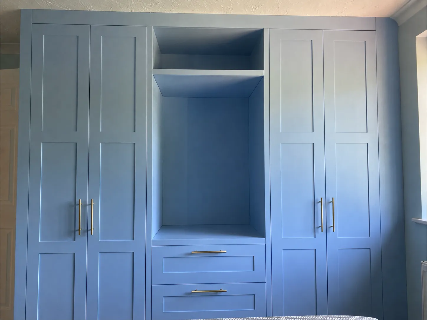 Built-in blue wardrobe with four doors, two drawers, shelf, and brass handles in a bedroom.