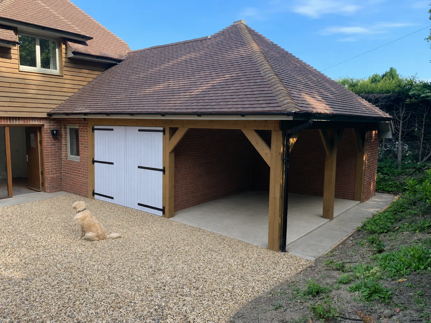 Wooden carport with tiled roof next to a brick house; golden retriever sitting on gravel driveway.