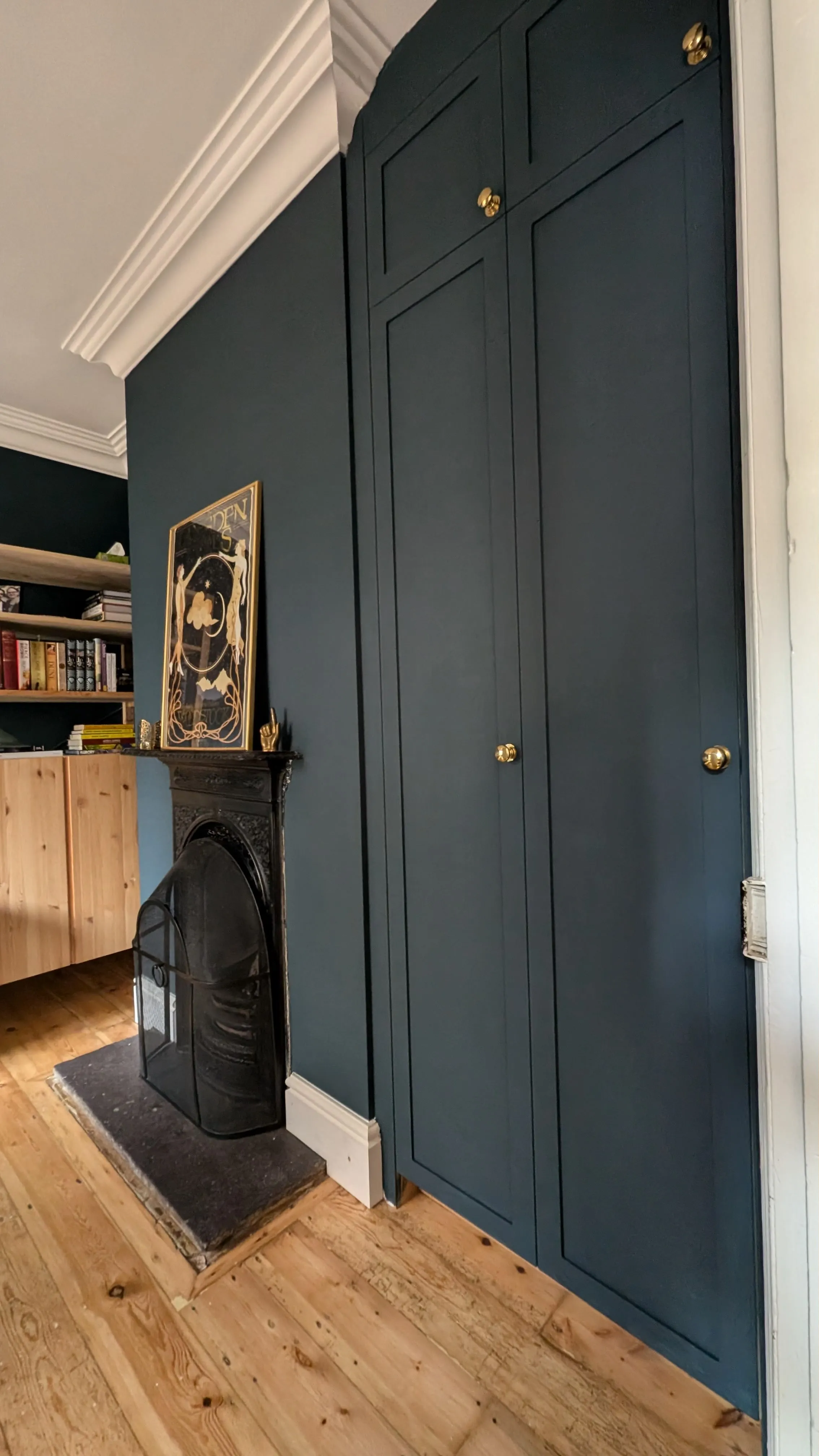 Dark blue built-in cabinets next to a black metal fireplace with wooden flooring and shelves with books.