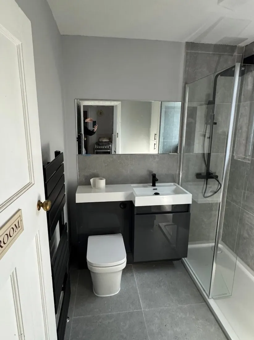 Modern bathroom with gray tiles, white toilet, black vanity with sink, glass shower, and black towel radiator.