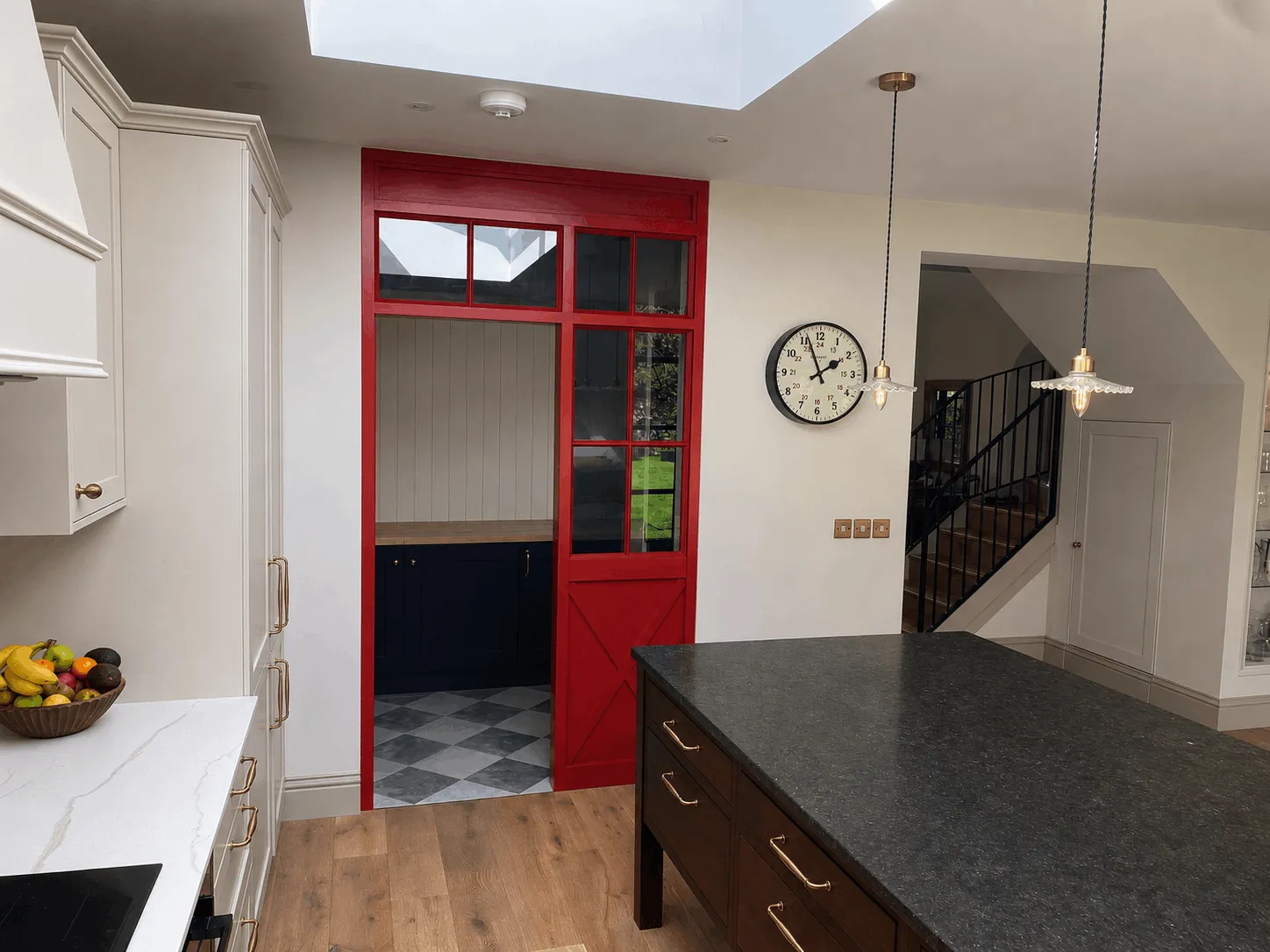 Modern kitchen with red door, wooden island with black countertop, white cabinets, and wall clock.
