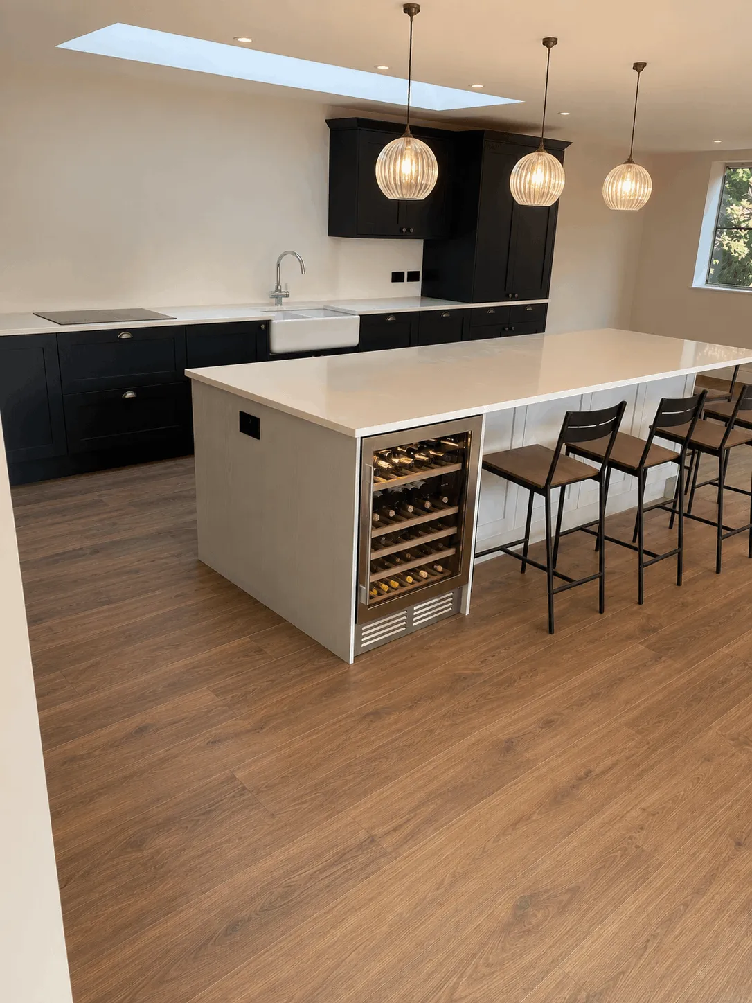 Modern kitchen with black cabinets, white island, wood floors, pendant lights, and a wine cooler.