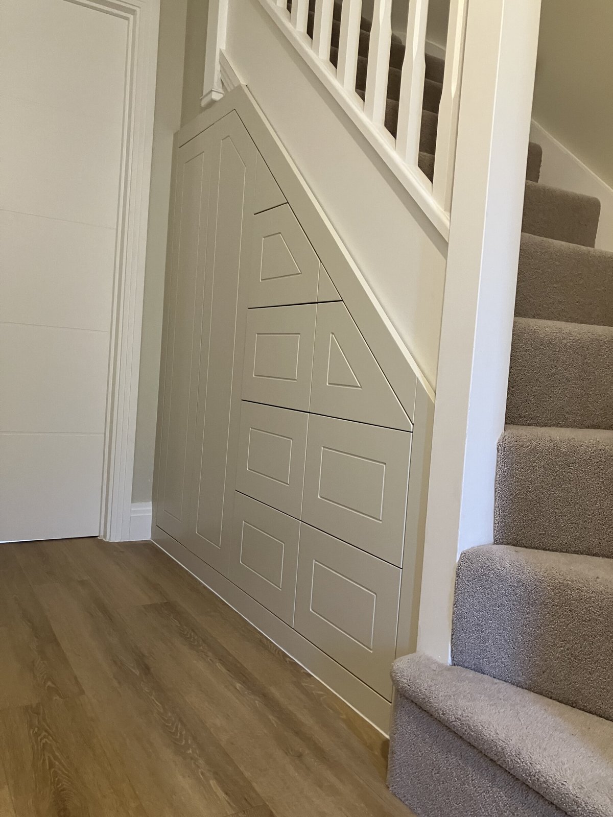 Fitted under-stairs storage with painted panelled doors and drawers, built to follow the line of the staircase.