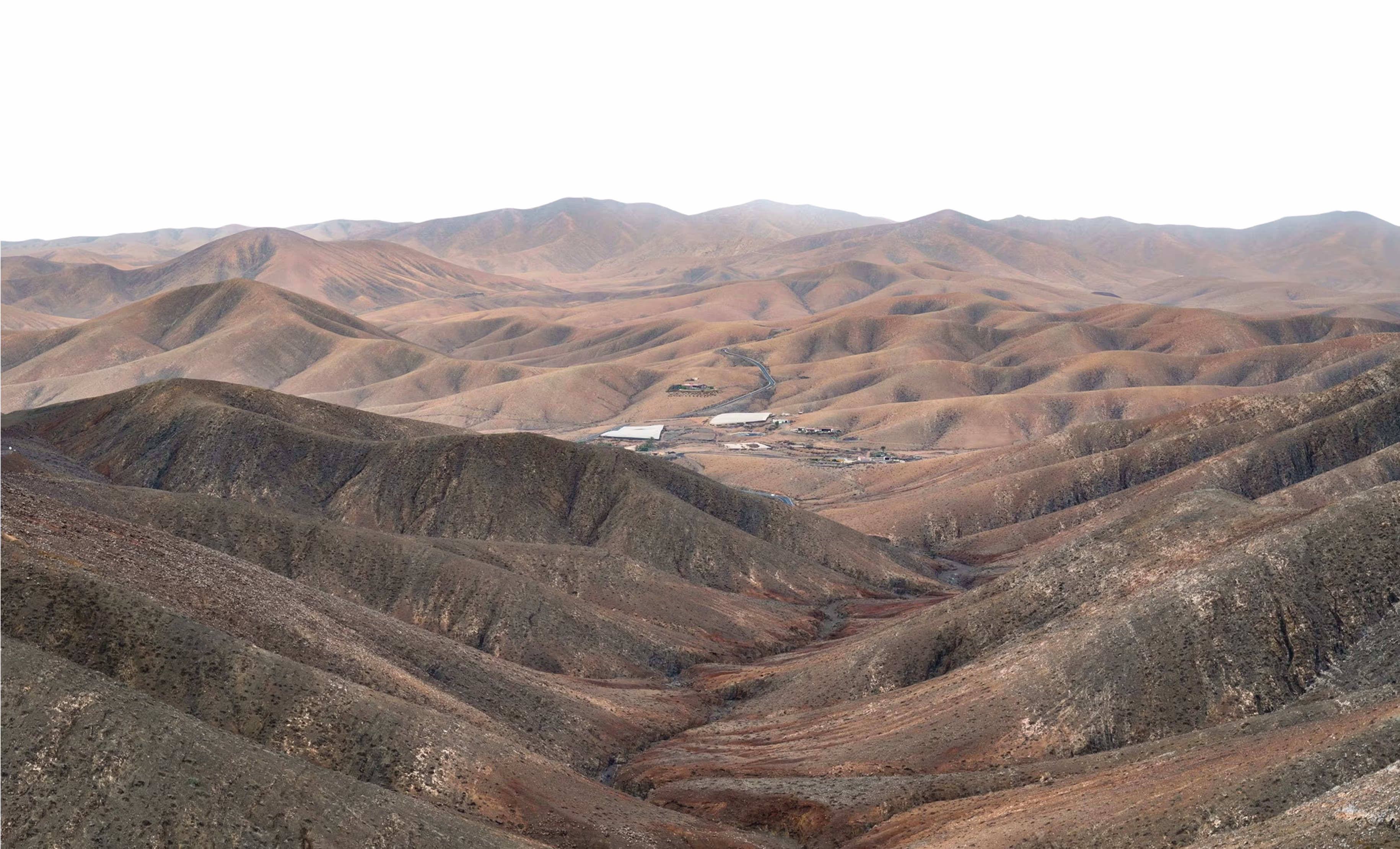 Expansive view of barren, rolling hills and a small cluster of buildings in the valley.