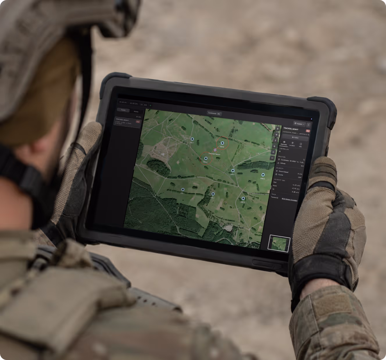Soldier holding a rugged tablet showing a digital map with multiple tracked locations.