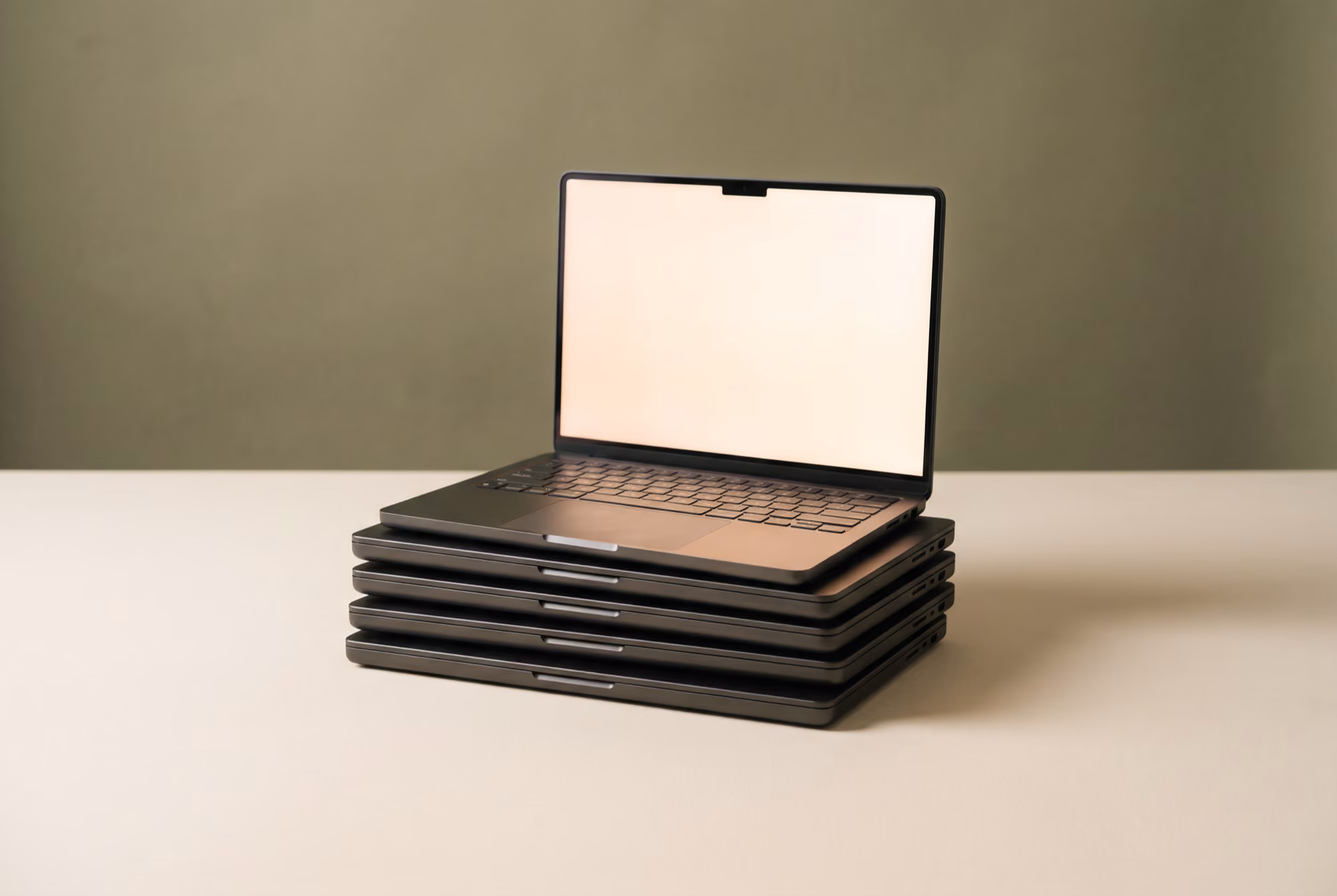 Stack of five closed black laptops with one open laptop on top with a blank screen.