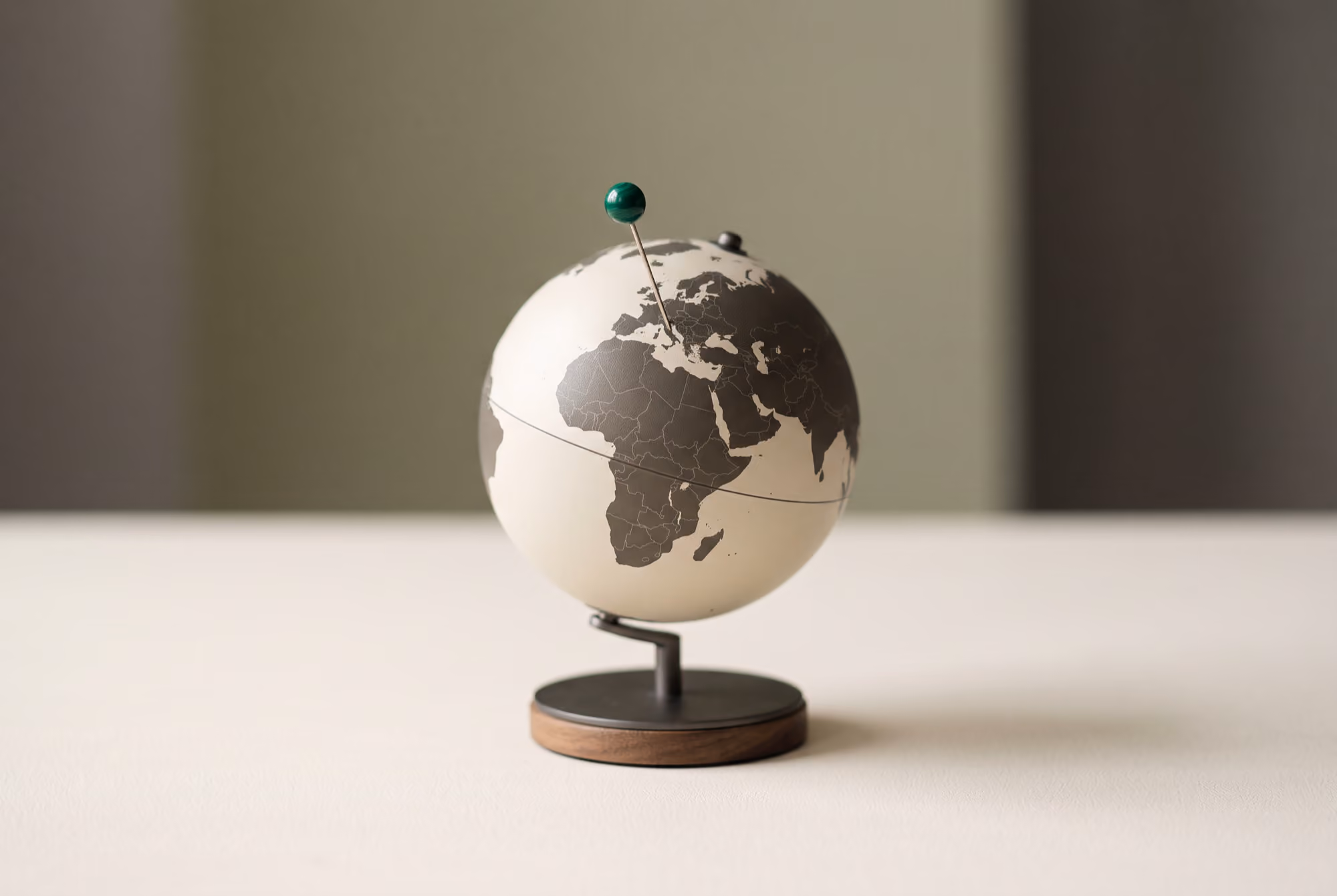 Small black and white globe with a green pin on Europe, on a wooden and metal stand.