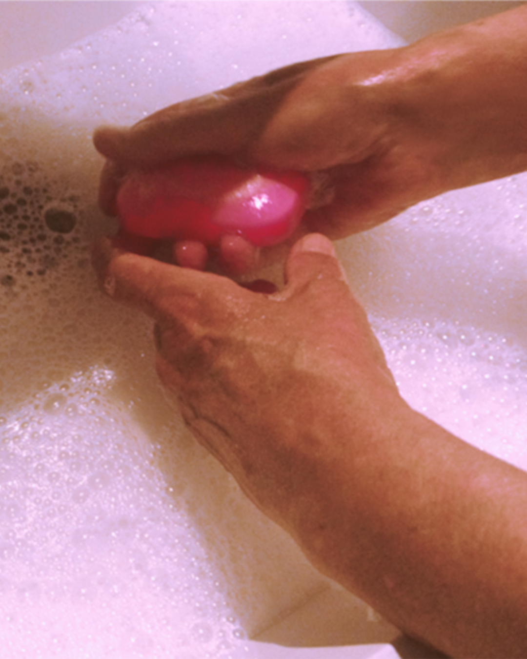 Person washing hands with a pink Eubos soap bar in foamy water.