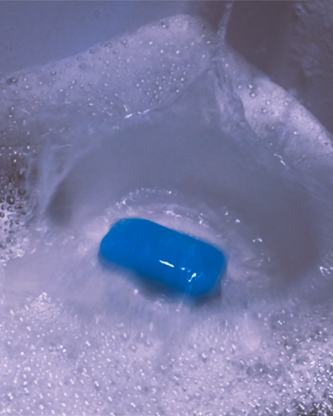 Blue Eubos soap bar floating in foamy bath water.