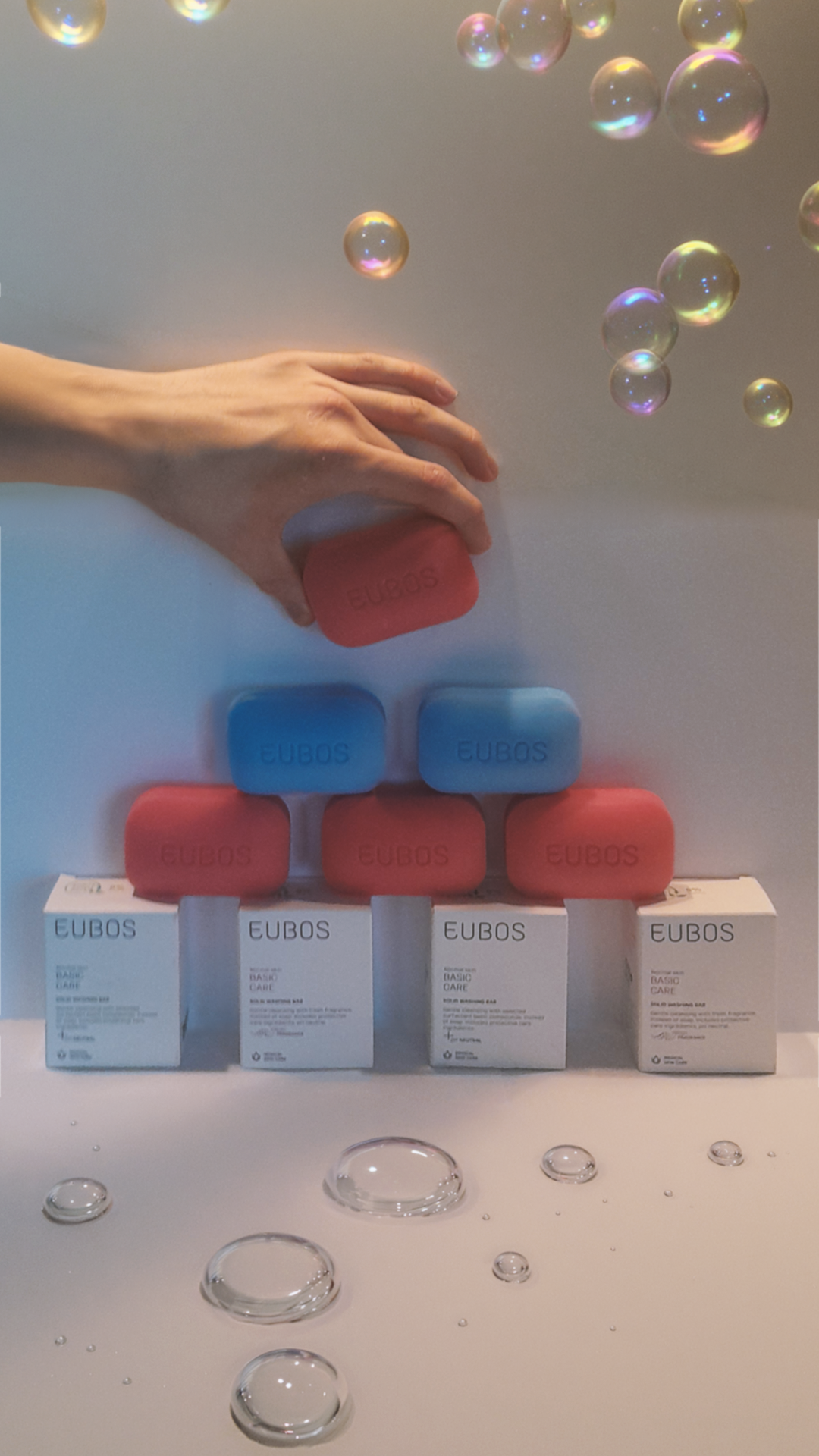 Hand reaching toward stacked Eubos soap bars and packaging with floating bubbles.
