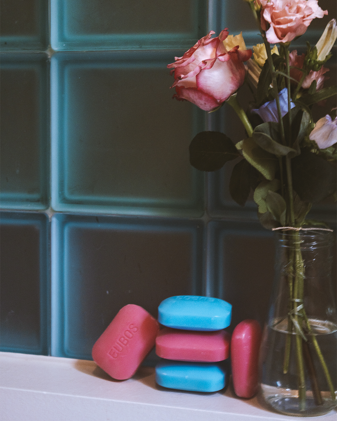 Eubos soap bars and flowers styled on a bathroom shelf with soft cinematic lighting.