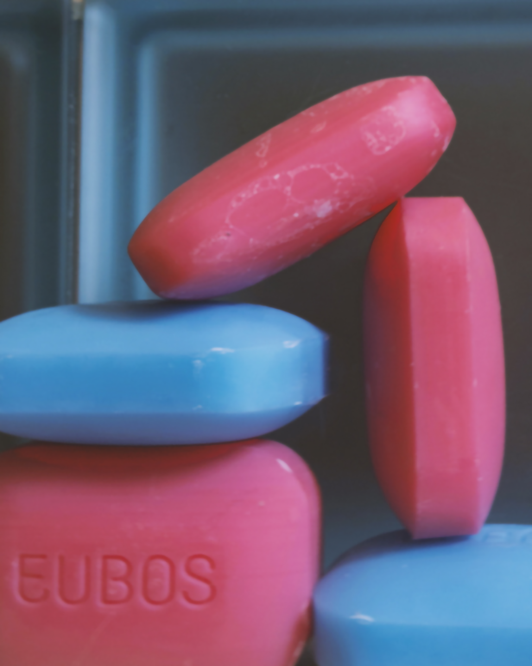 Stacked pink and blue Eubos soap bars against dark bathroom tiles.