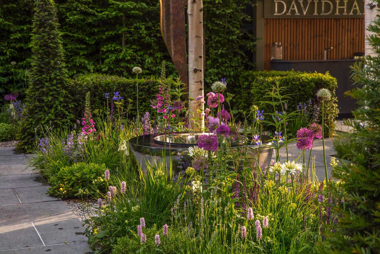 Reflective metal water feature surrounded by flowering shrubs in a Chelsea Flower Show garden