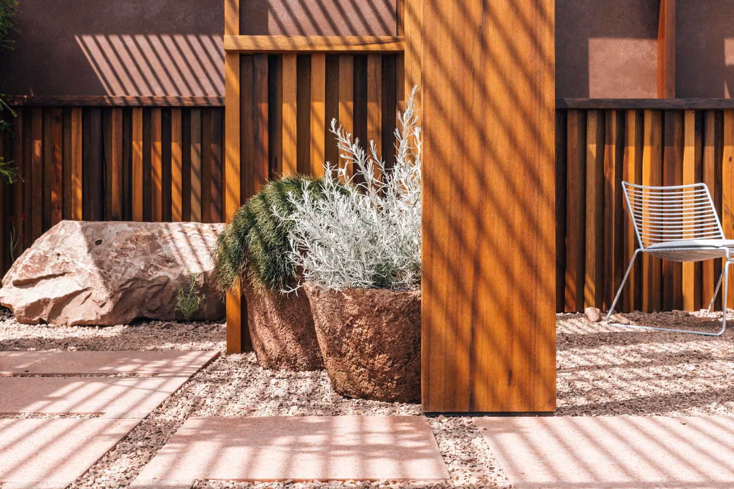 Sunlit courtyard garden with a timber slat screen, stone planters and gravel paving