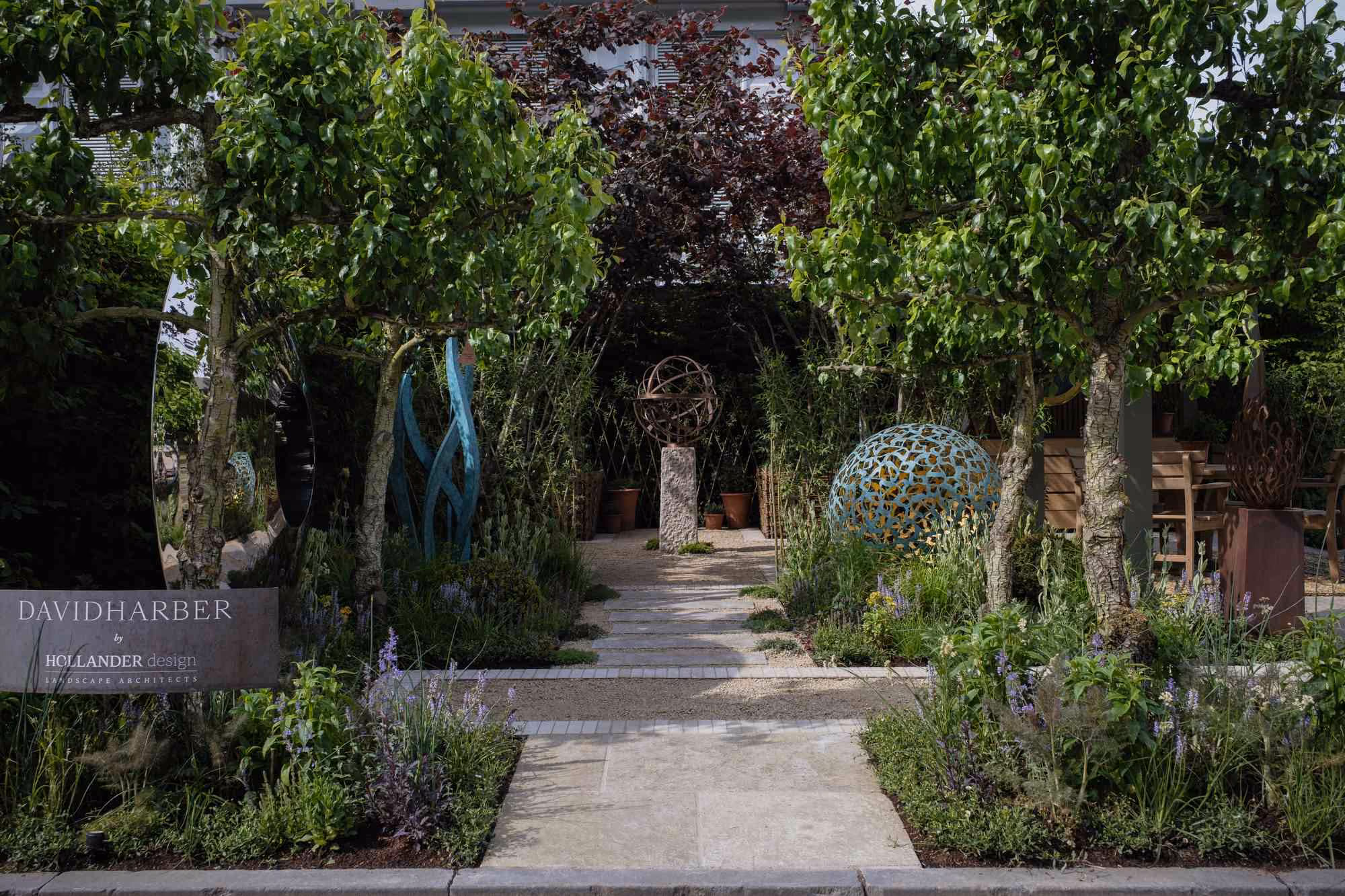 Show garden pathway with a spherical blue metal artwork and a central armillary sphere among trees