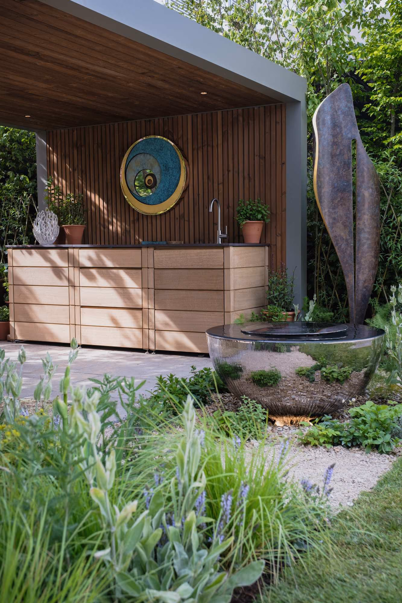 Outdoor kitchen with timber cabinets, a sink and a circular reflective water feature in a show garden