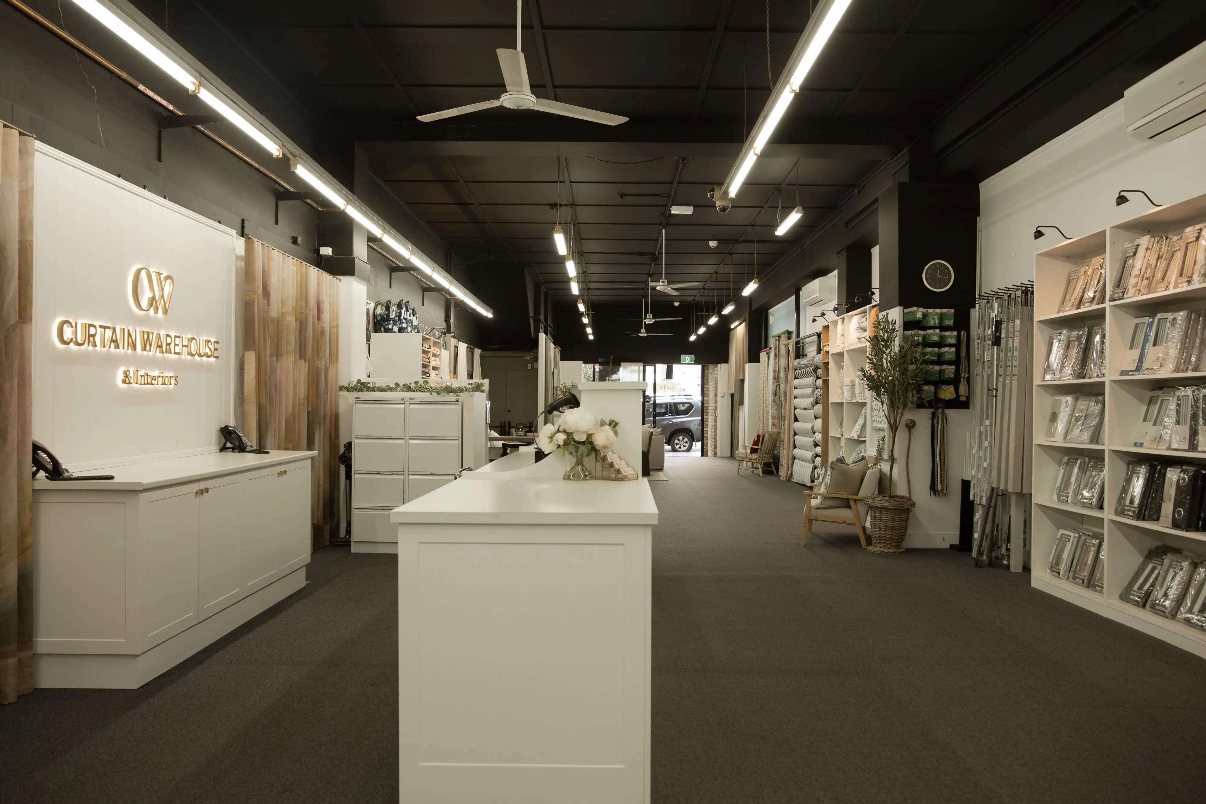 Interior of Curtain Warehouse showroom with white display counters and curtain samples on shelves and racks.