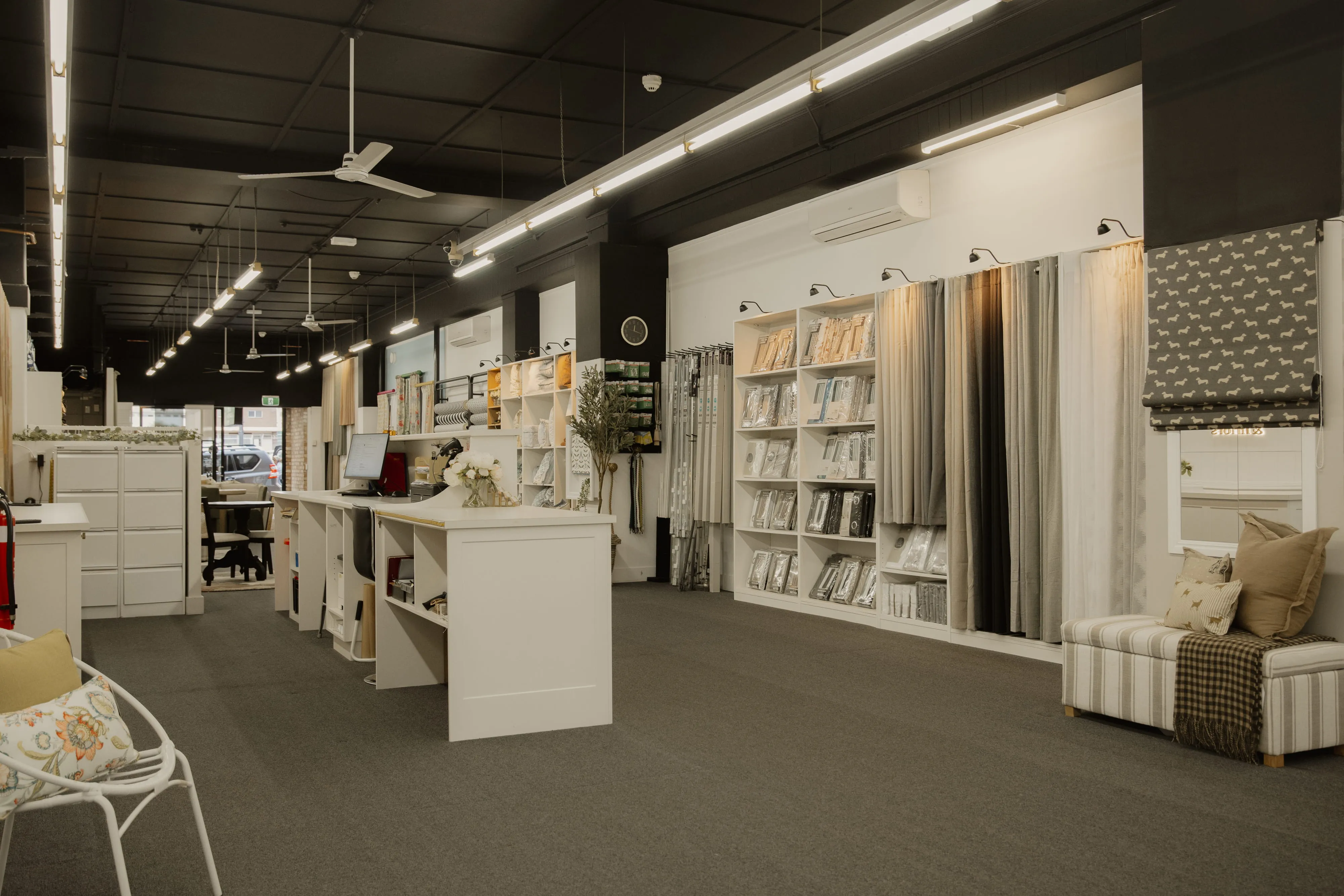 Interior of a curtain showroom with white shelves, sample curtains, and a seating area with pillows.