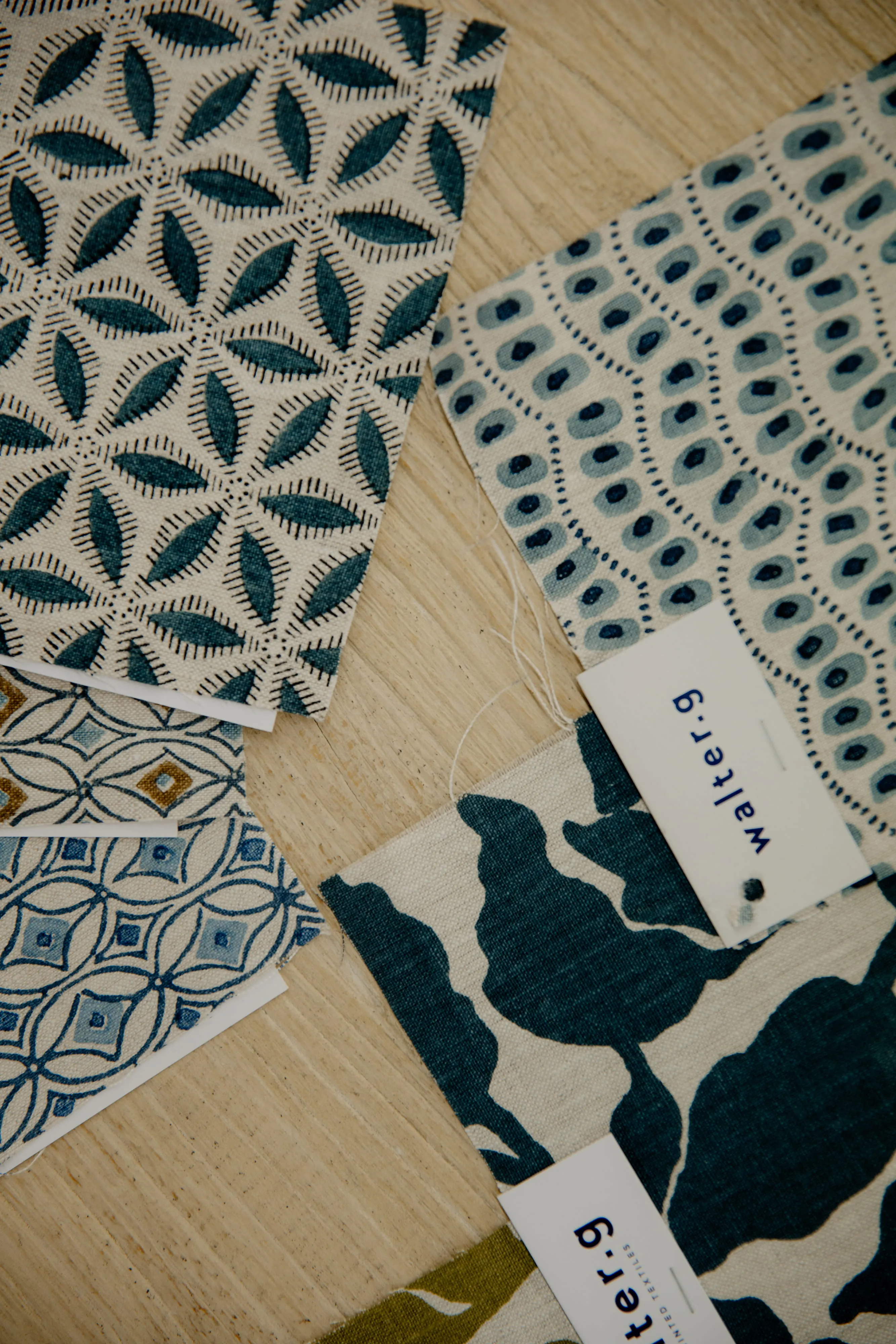Various blue and white fabric swatches with geometric and leaf patterns on a wooden surface.