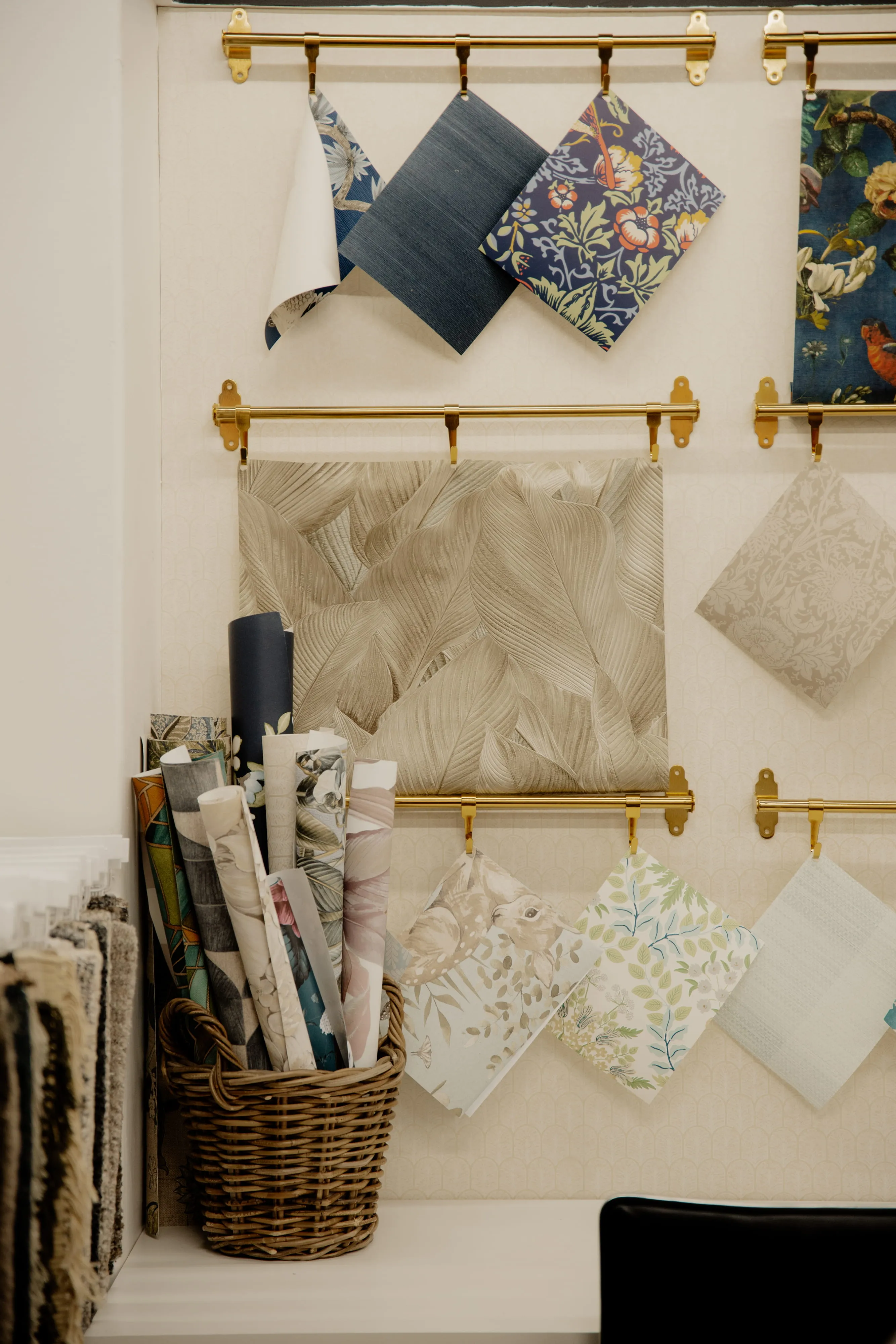 Various fabric and wallpaper samples displayed on gold racks and rolled in a wicker basket indoors.