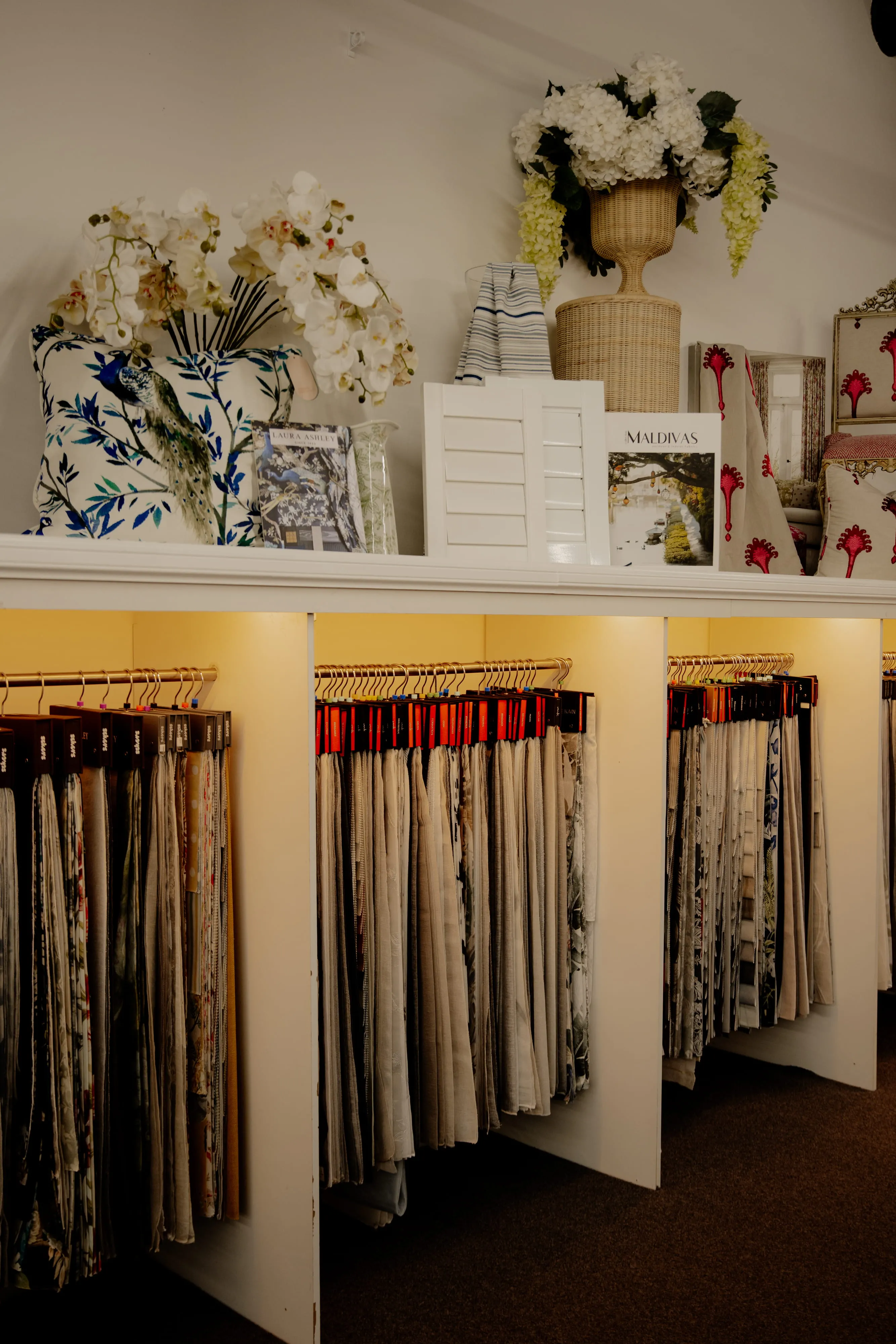 Display of fabric samples hanging under shelf with floral pillows and decorative items on top.