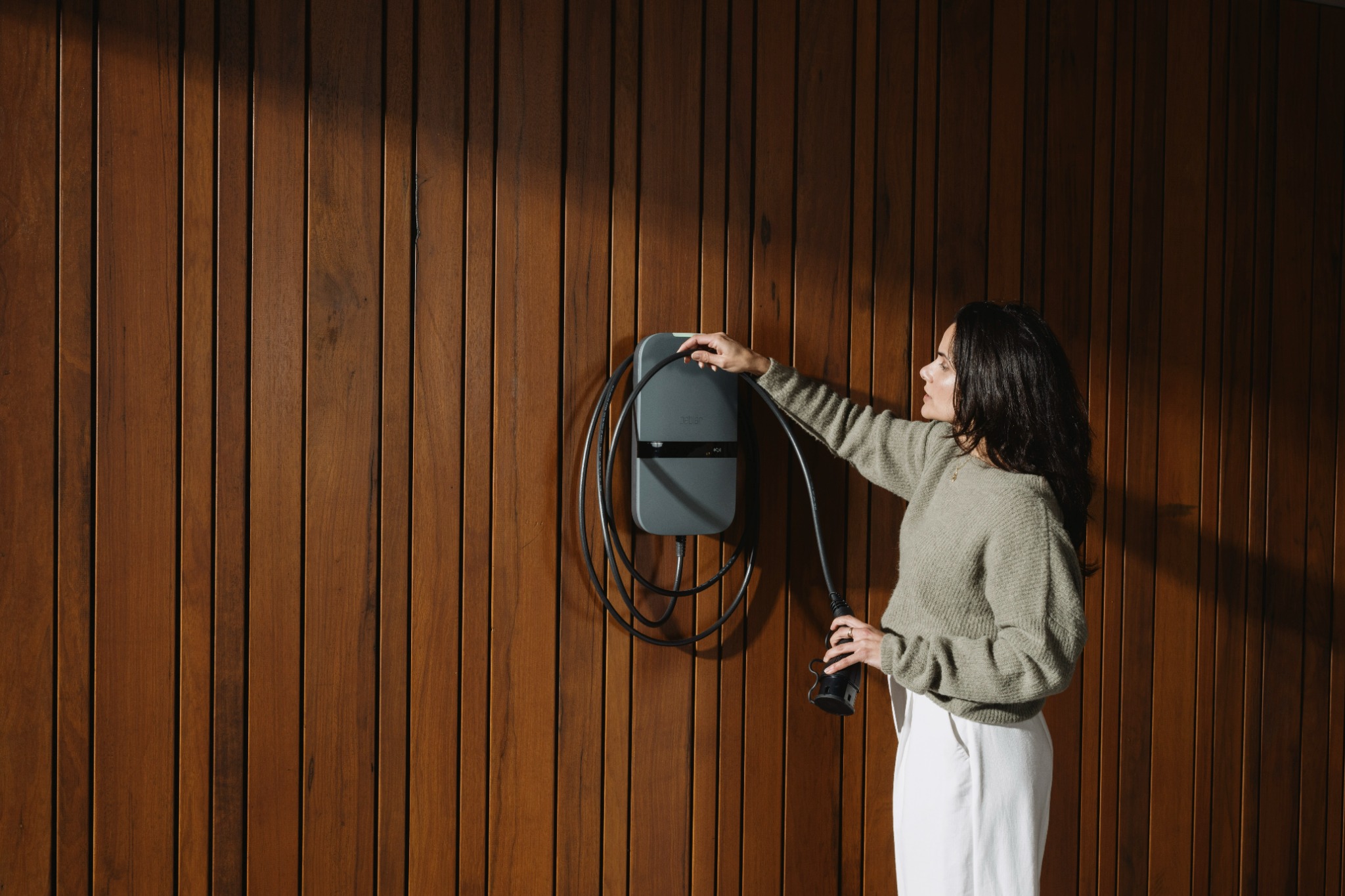 Vrouw pakt de laadkabel van een Peblar-laadpunt aan een houten gevel