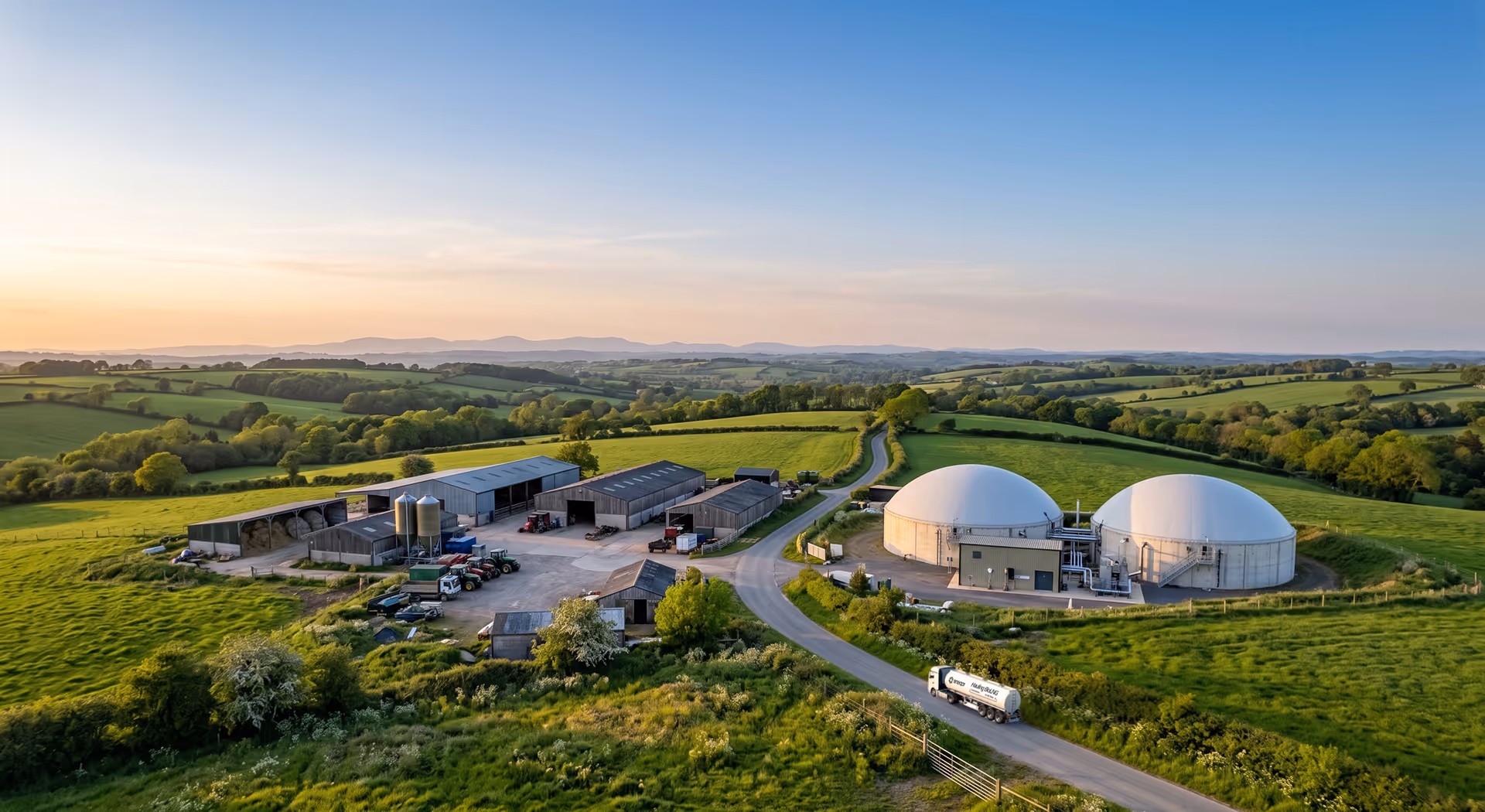 Aerial view of a farm with large storage tanks, barns, tractors, and green fields under a clear sky.