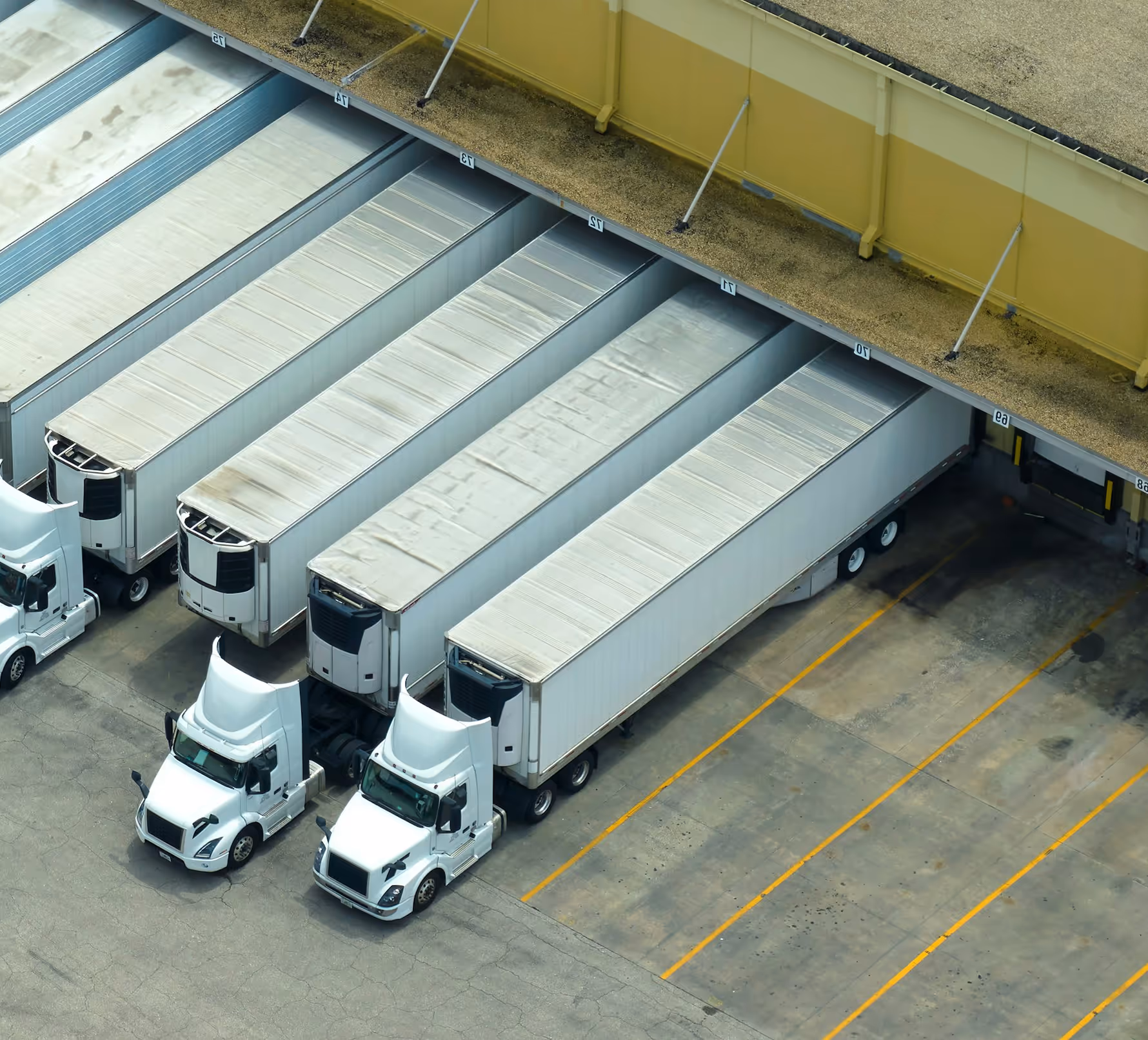 Aerial view of white semi trucks backed into warehouse loading dock bays 10 to 15.