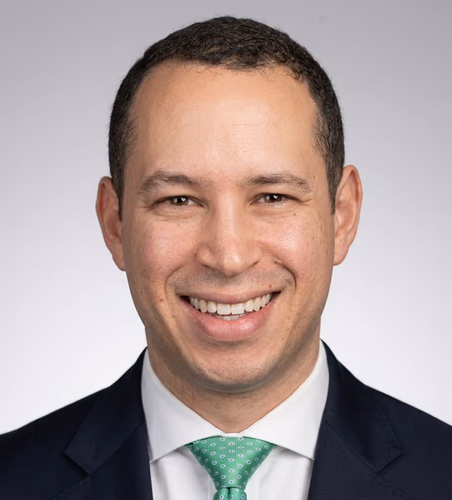 Smiling man with short dark hair wearing a white shirt, green tie, and dark suit jacket.