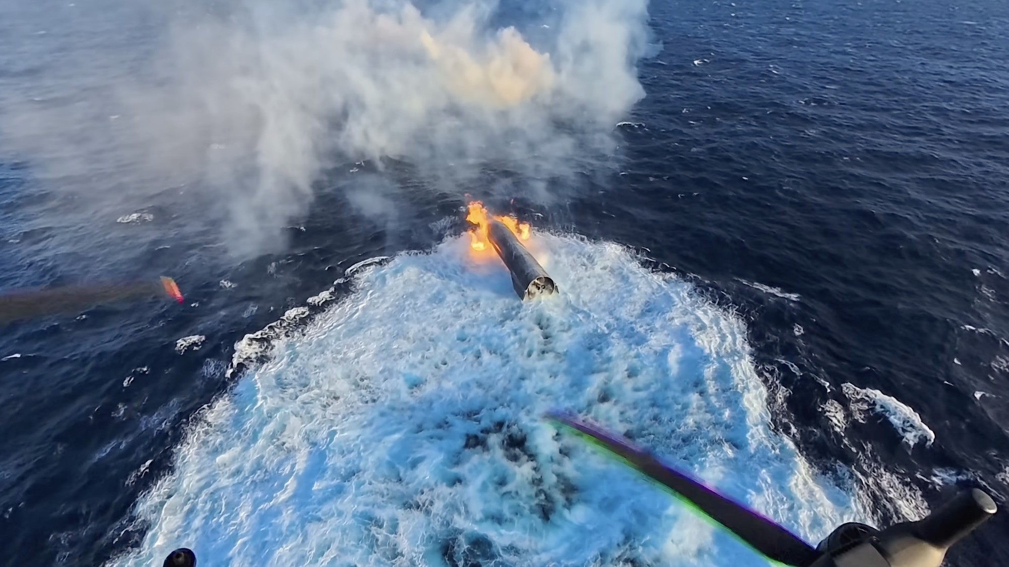 A SpaceX Super Heavy booster floating on the ocean after splashdown, still burning at the engine section