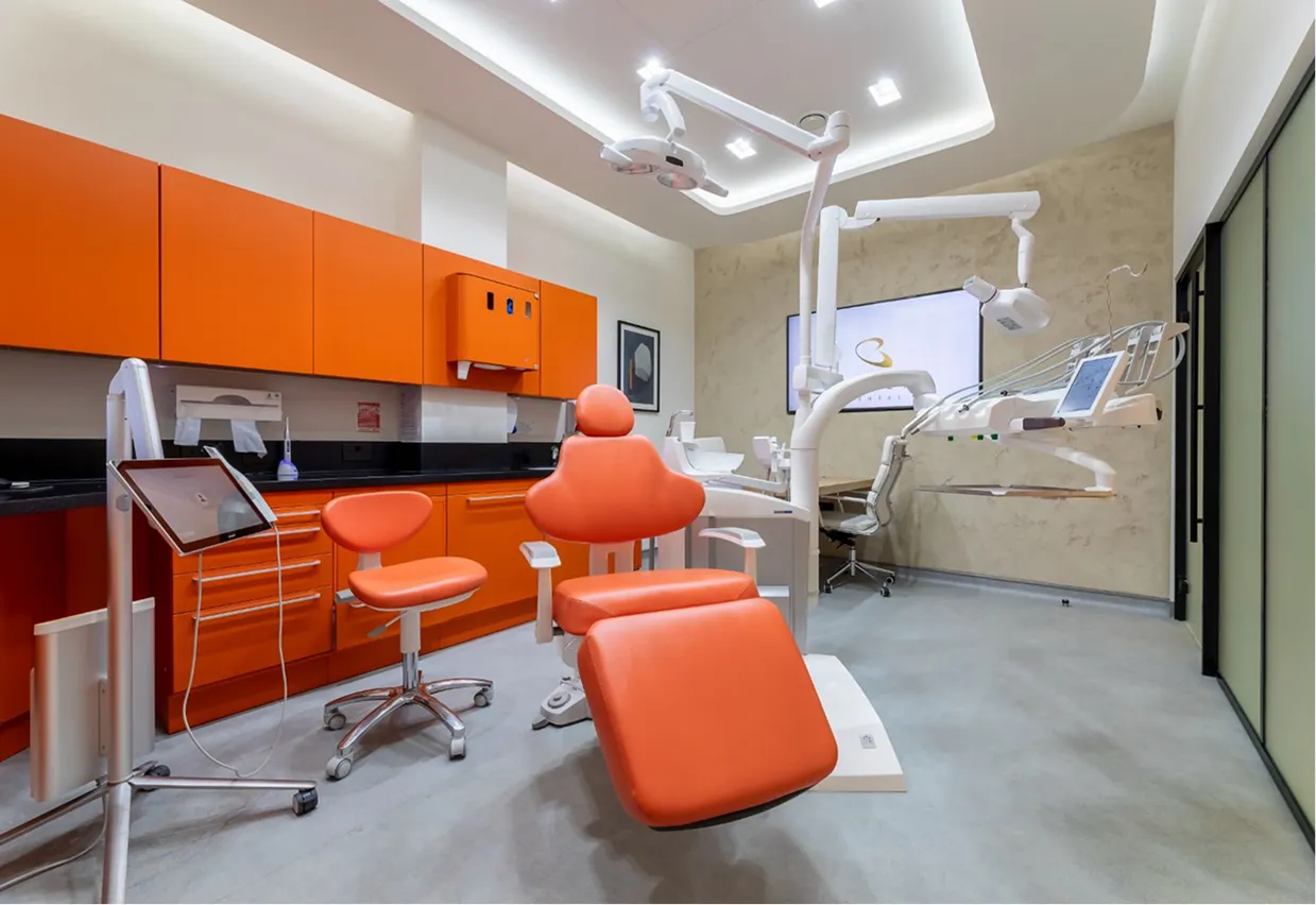 Modern orange-themed dental treatment room with chair and overhead light
