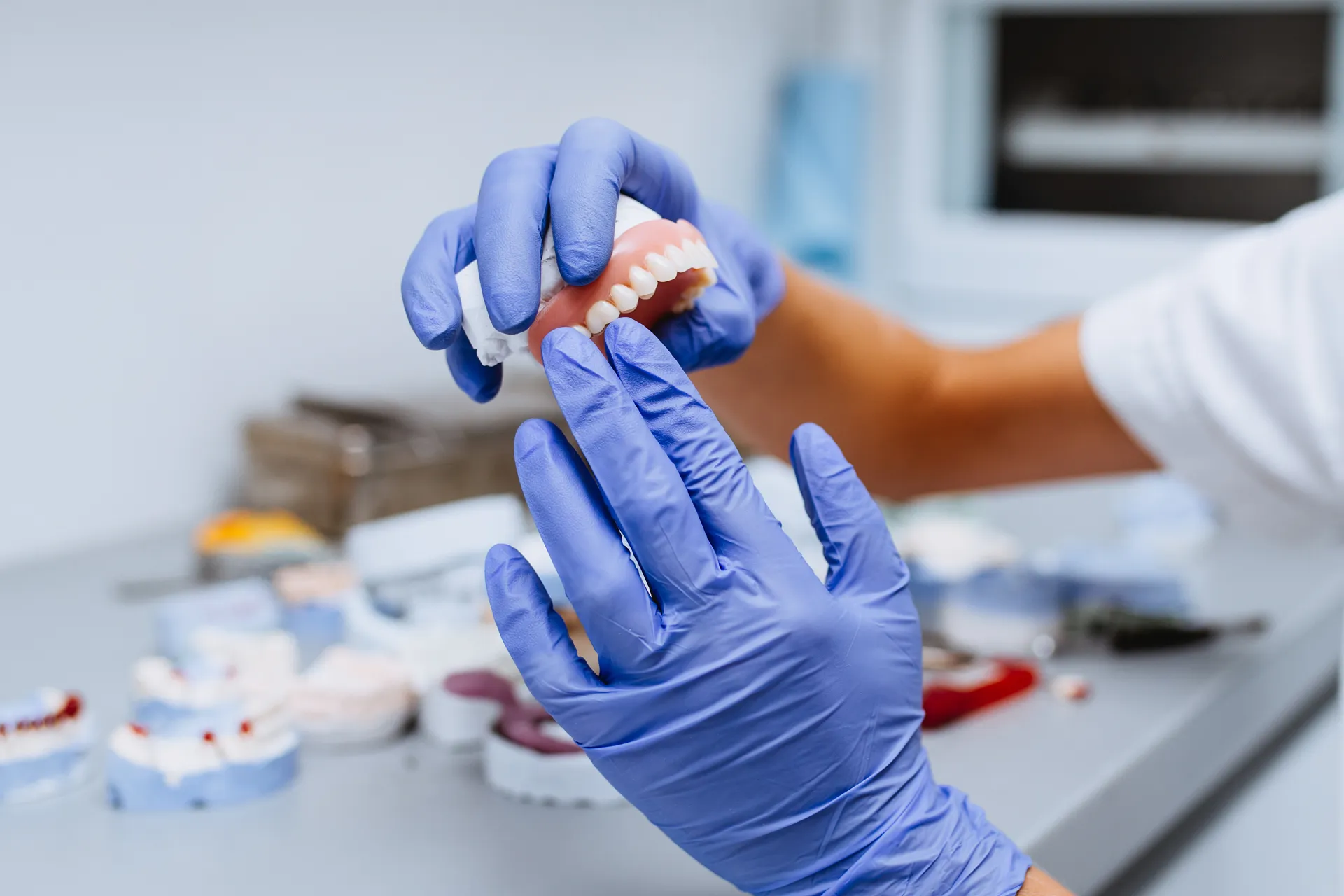 Gloved hands holding a denture in a dental laboratory