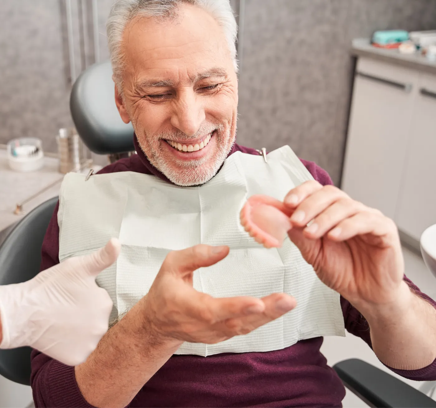 Smiling elderly patient in the dental chair being shown a denture