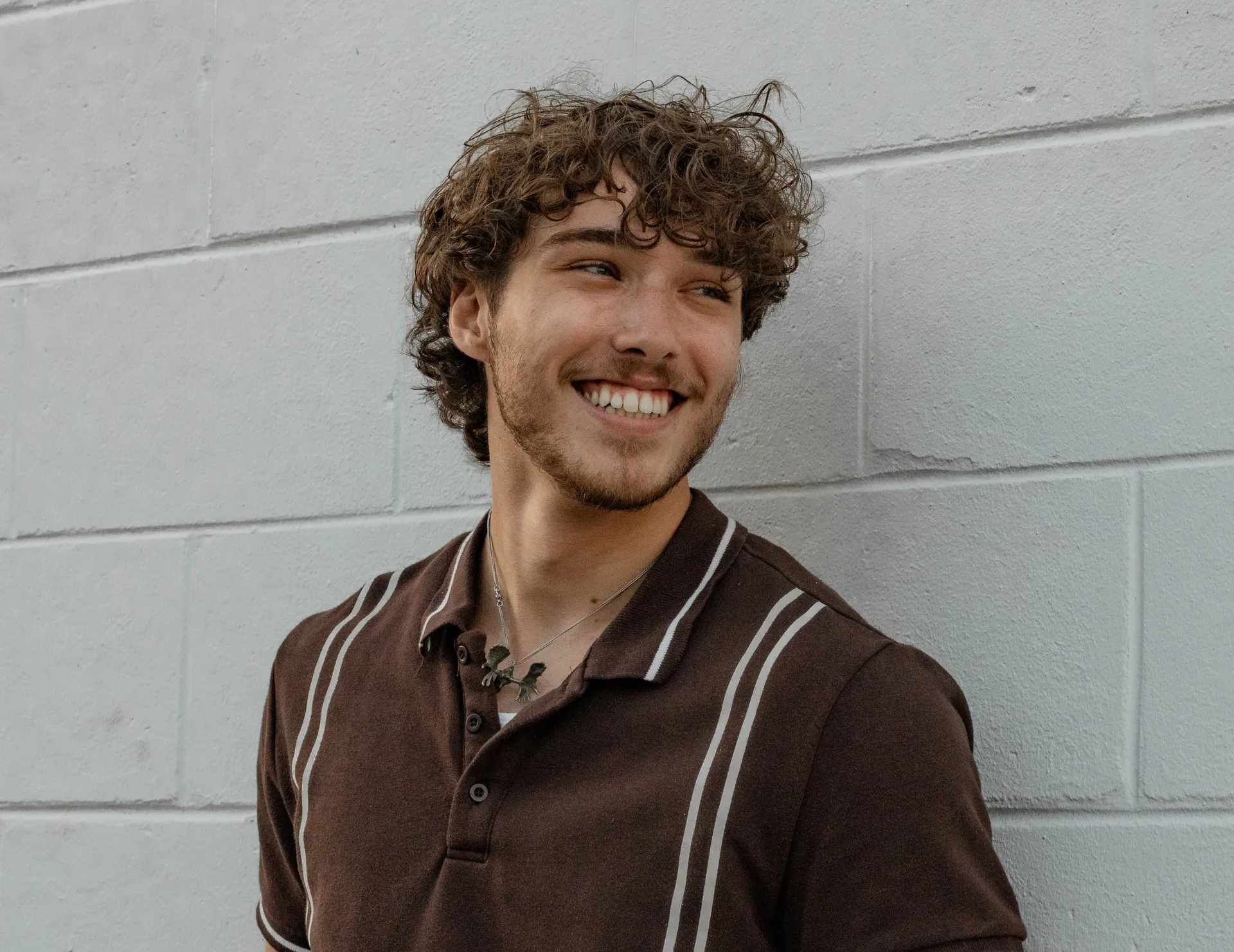 Young man with curly hair smiling broadly against a wall