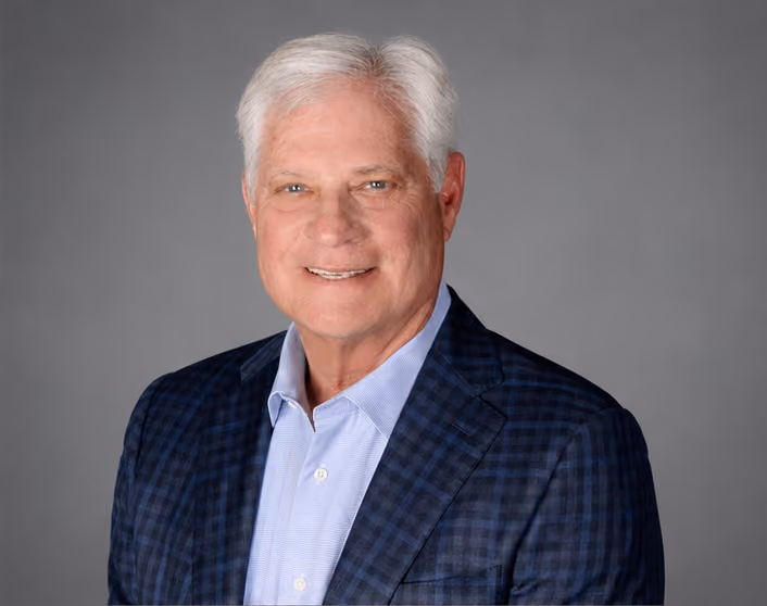 A headshot of Stew Atkinson wearing a blue checkered jacket and light blue shirt smiling against gray background.