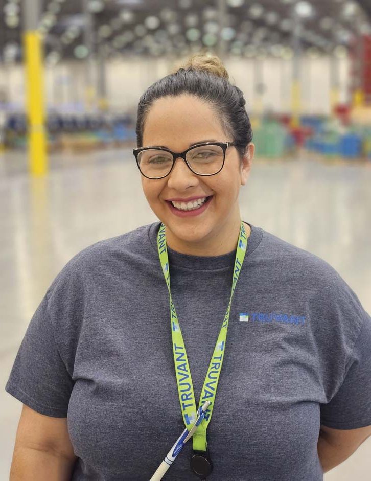 A smiling Truvant employee wearing a lanyard in a warehouse