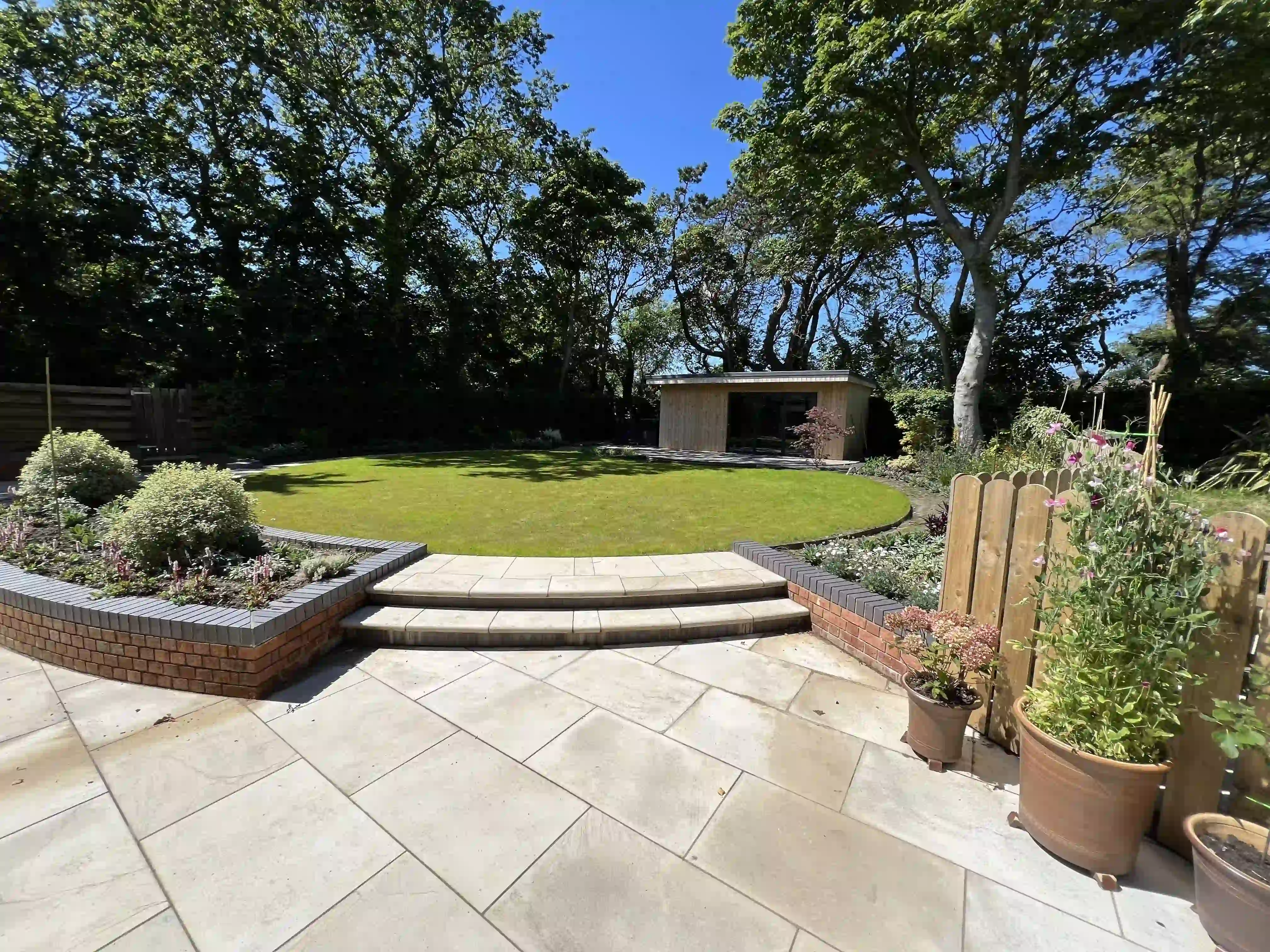 Curved sandstone steps leading from the patio to a circular lawn and garden room at 15 The Links, Peel
