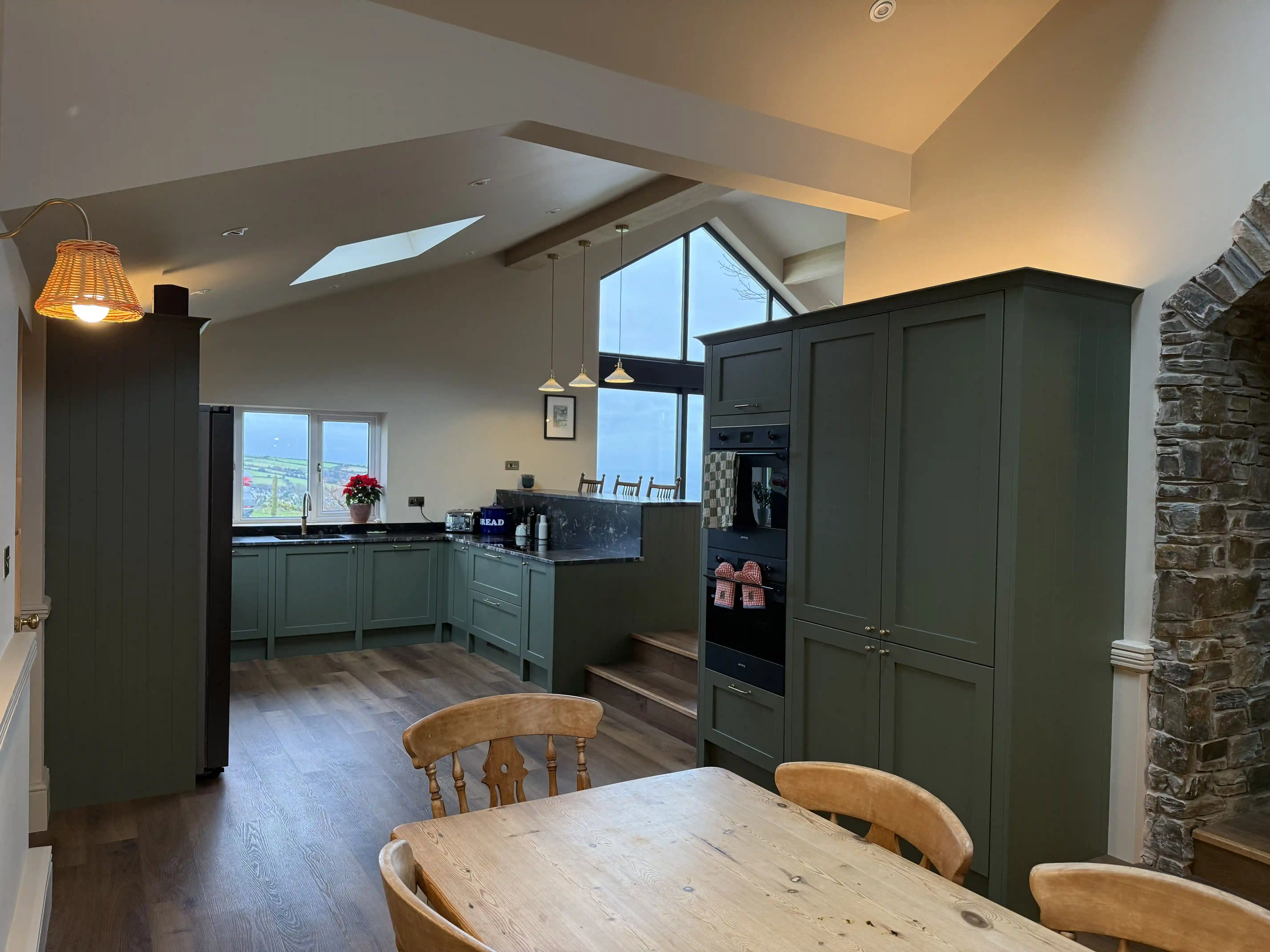 Kitchen with tall green units and exposed stone archway at Ballamillighyn Cottage, Laxey