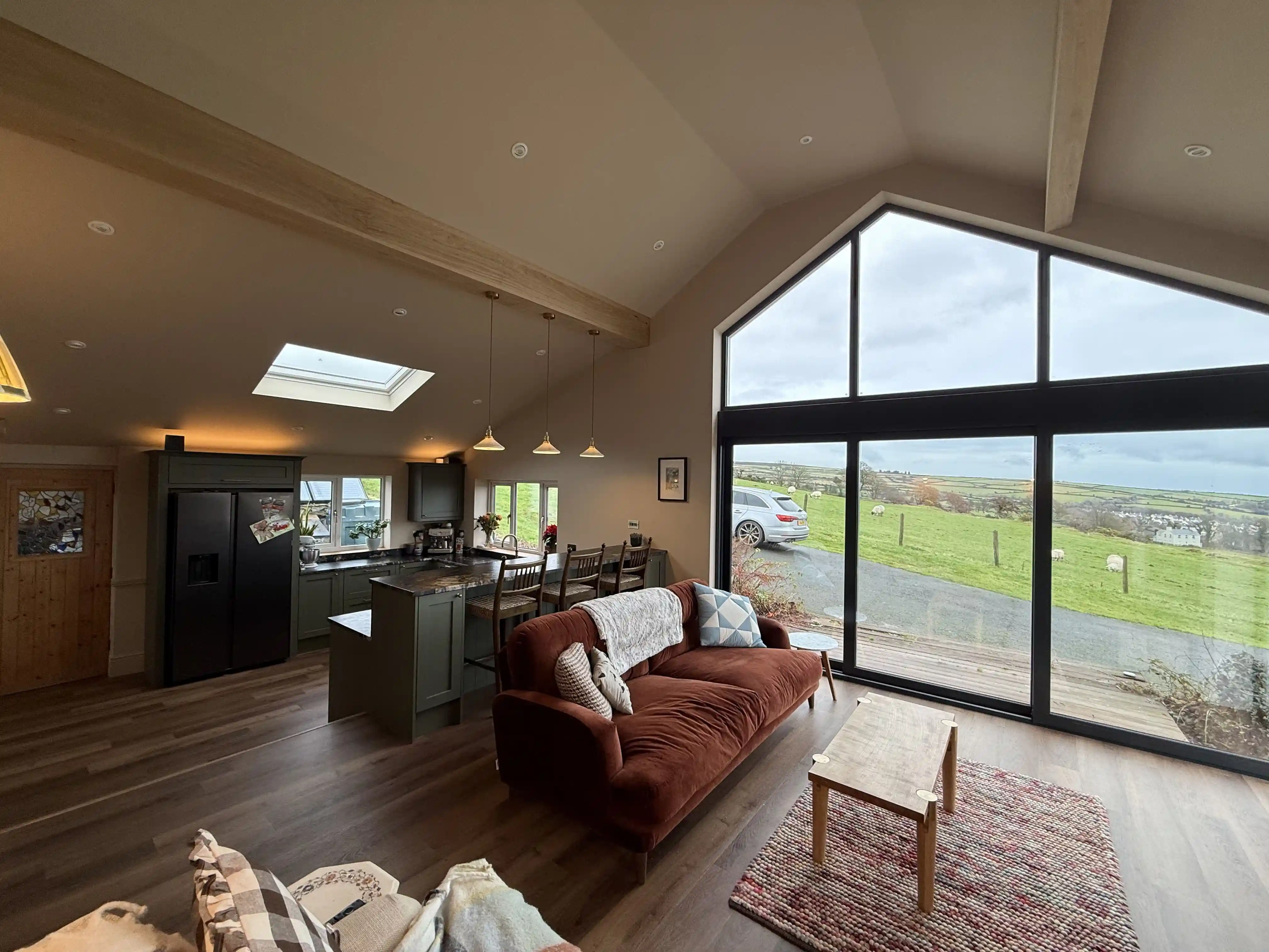Living area with full-height gable glazing looking over fields at Ballamillighyn Cottage, Laxey