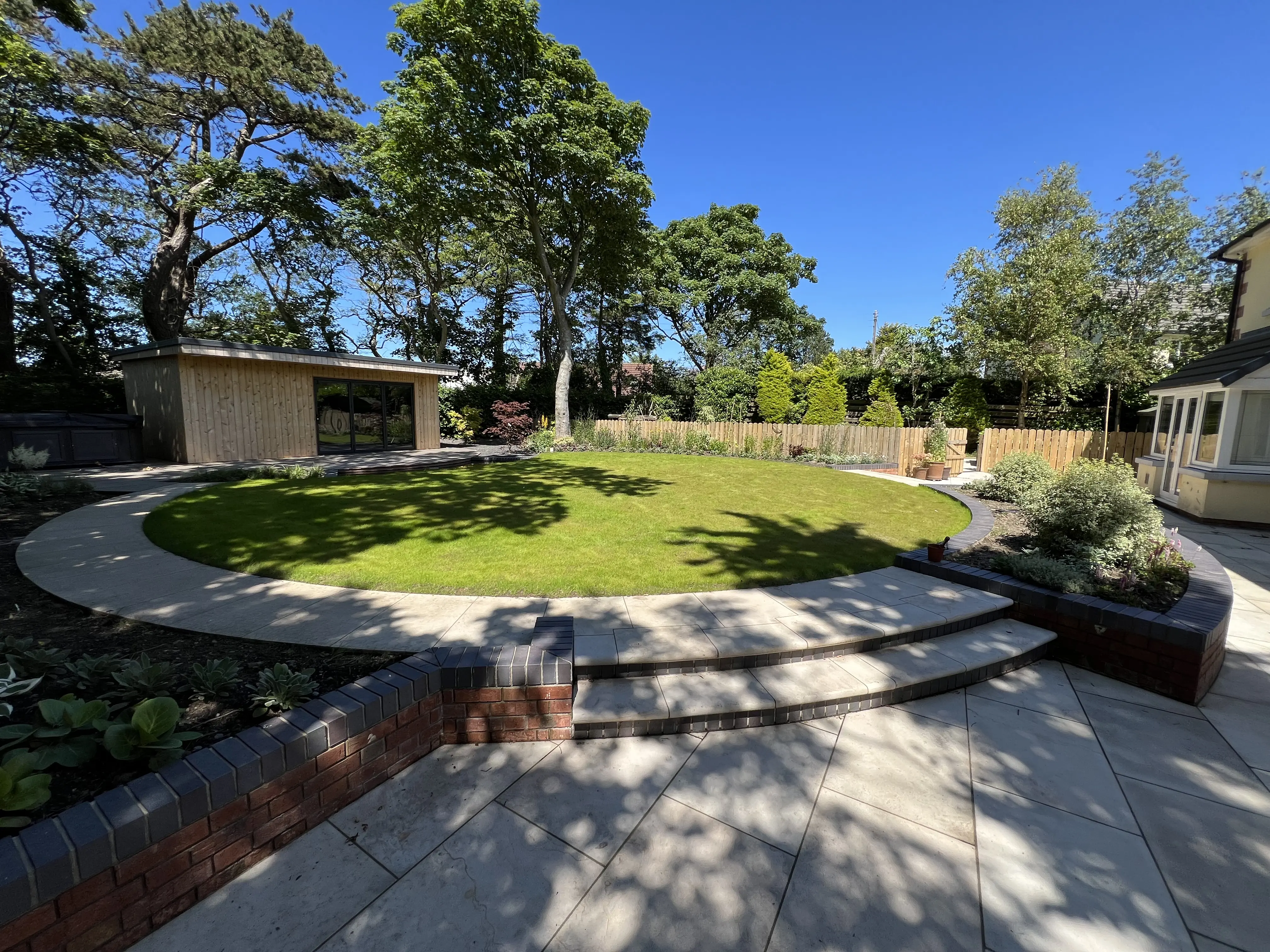 Circular lawn with curved paving edge, planting and garden room at 15 The Links, Peel