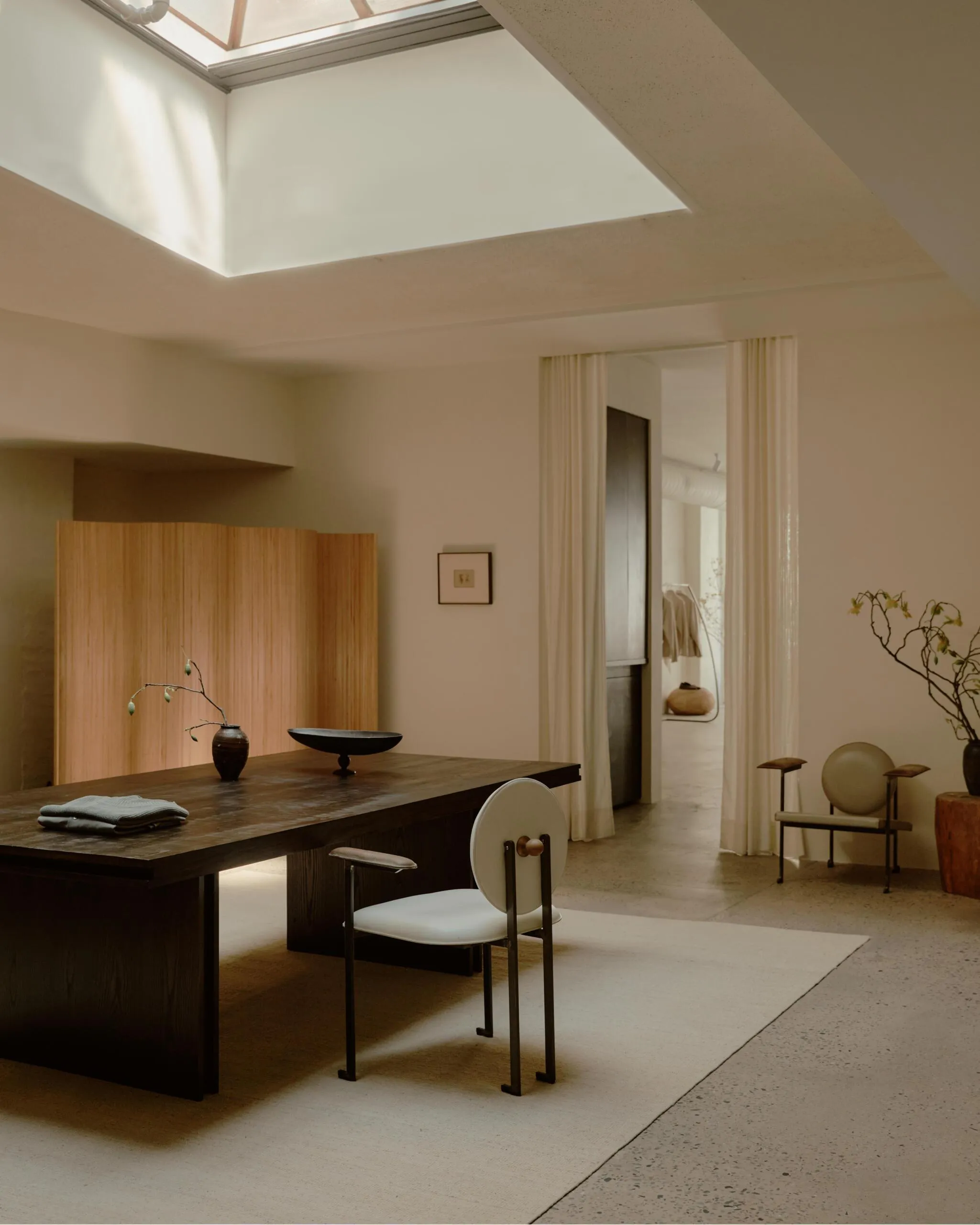 Minimalist Raum mit großem Holztisch, Designstühlen und natürlichem Licht durch Oberlicht.