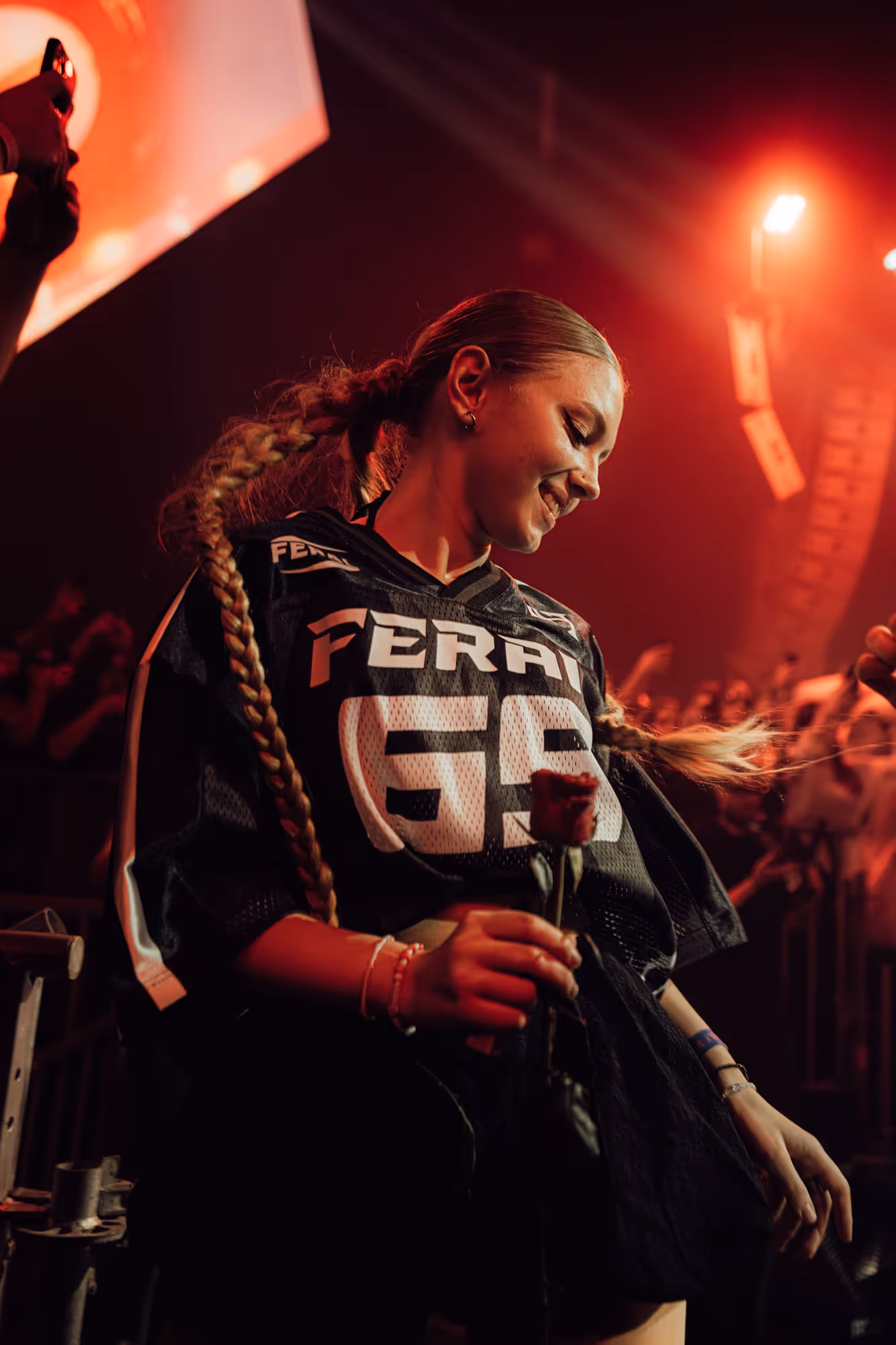 Smiling woman with long braided hair holding a red rose and dancing in a dimly lit club.