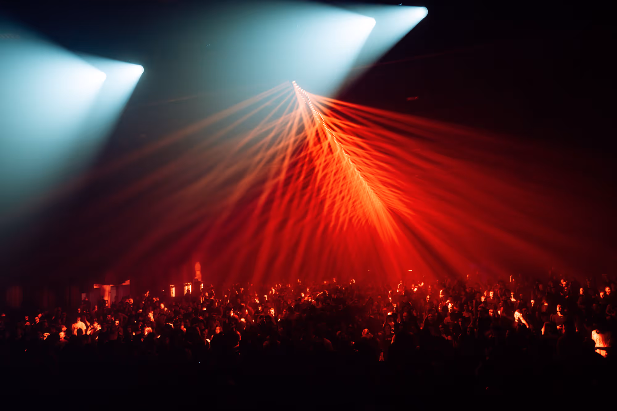 Large crowd illuminated by red and white stage lights at a nighttime event or concert.