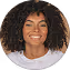 Smiling woman with curly hair wearing a white top against a plain background.
